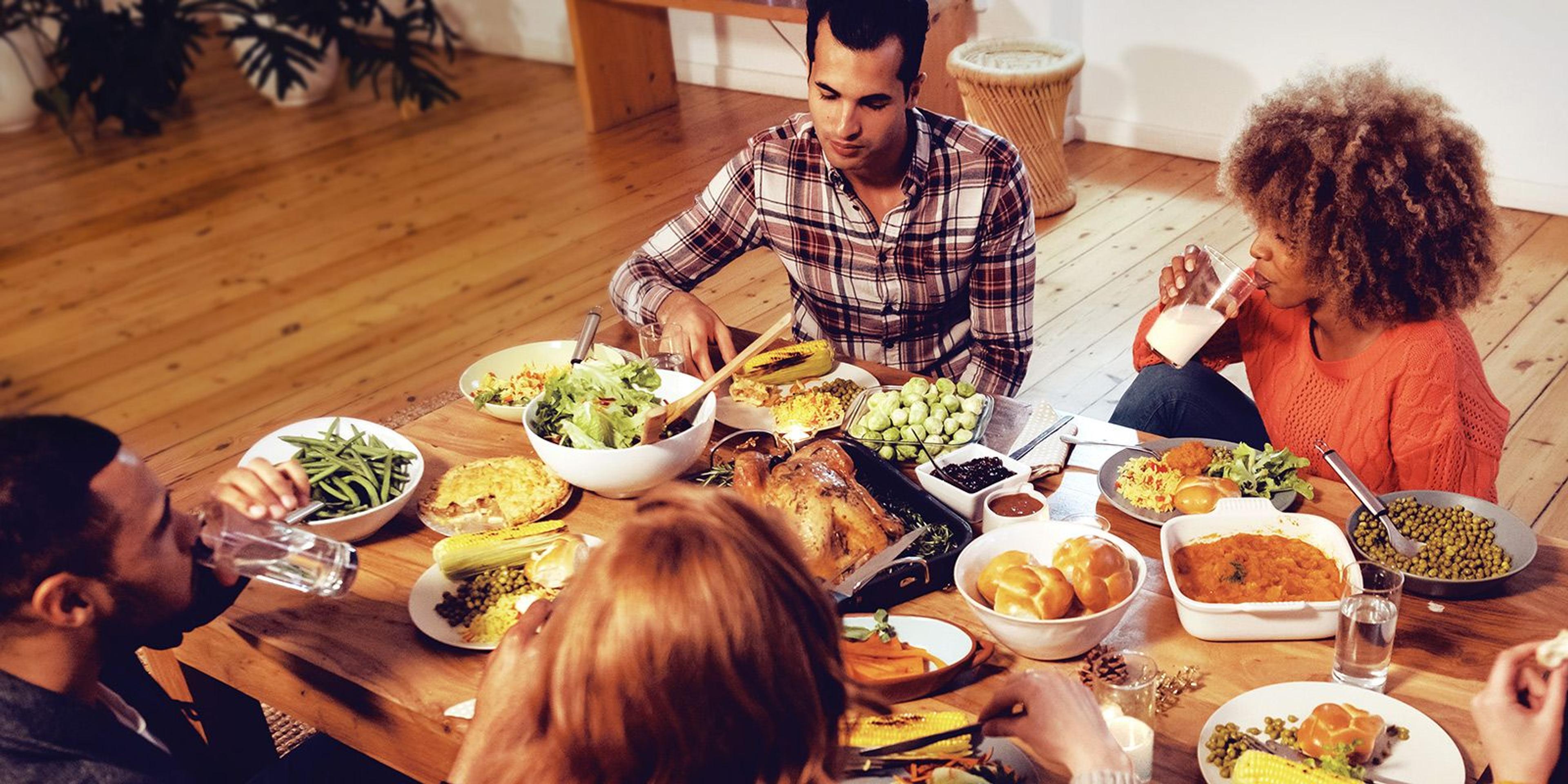 Diverse group of friends gather around table for Thanksgiving meal.