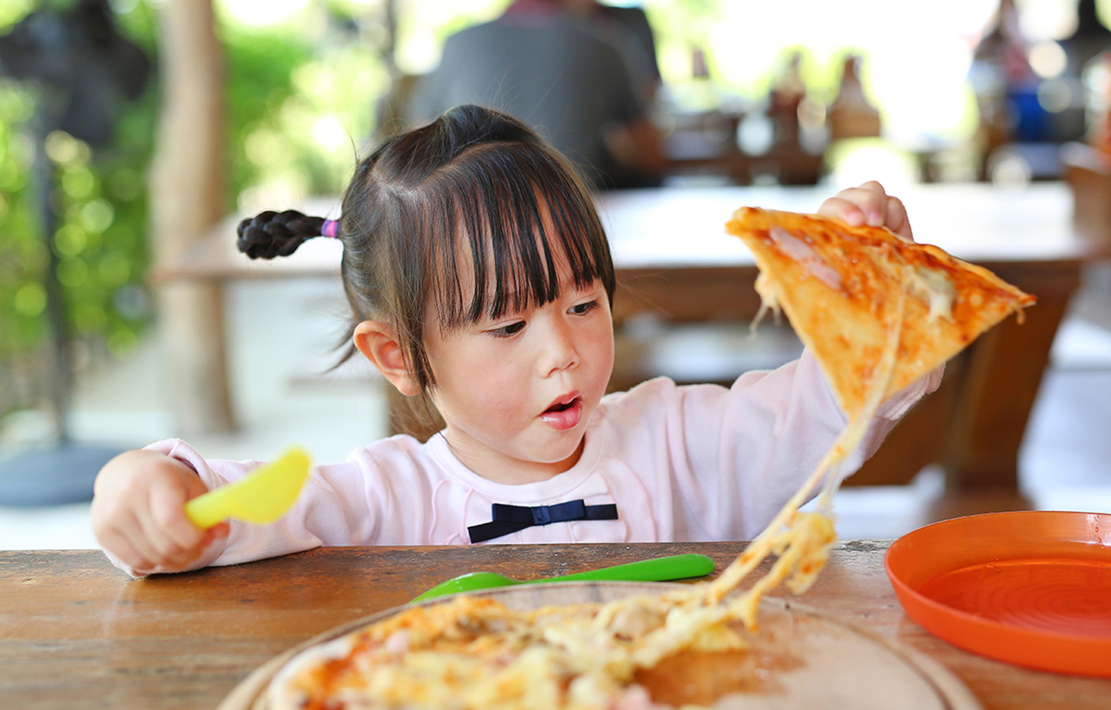 Young Asian girl grabs a piece of cheesy pizza.