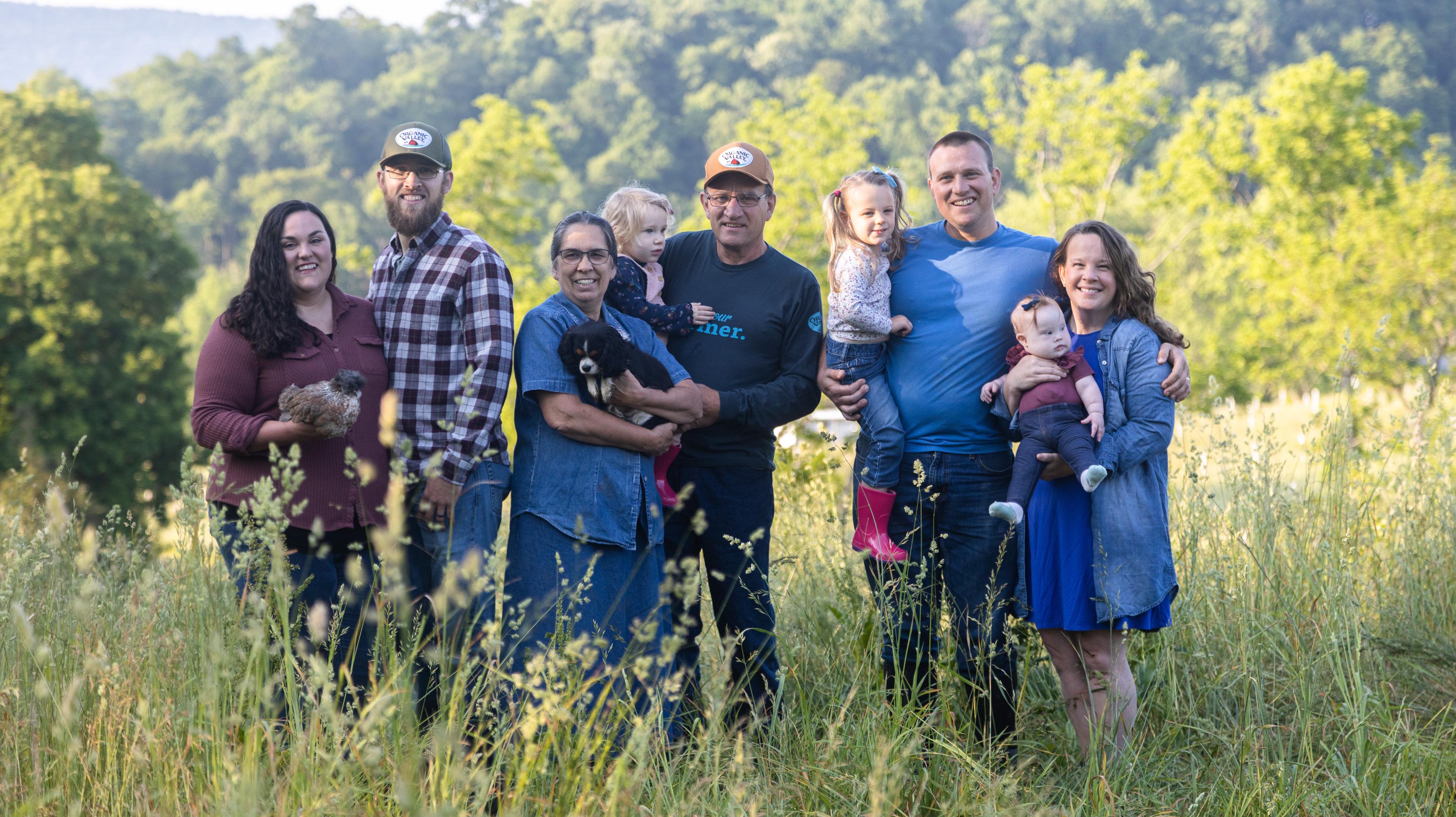 Members of the Ranck family pose in a field of grasses with trees in the background. One woman holds a dog and another holds a bird.