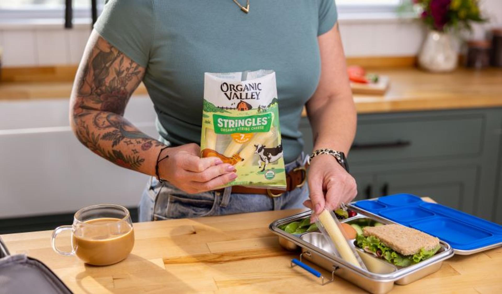 A woman places a string cheese in a bento box.