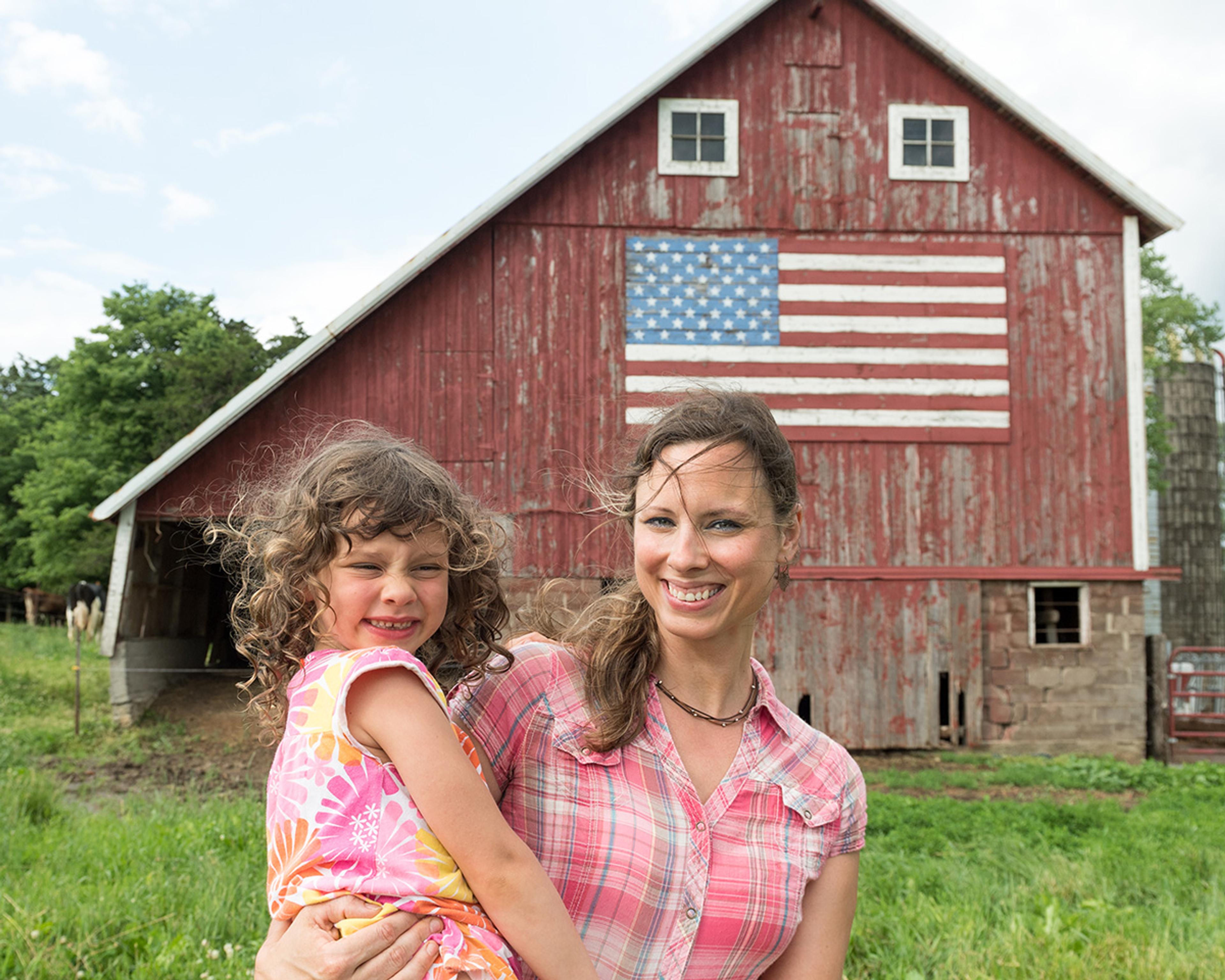 Mom Heidi Vosberg holds daughter Rachel in front of their red barn with an American flag painted on it.