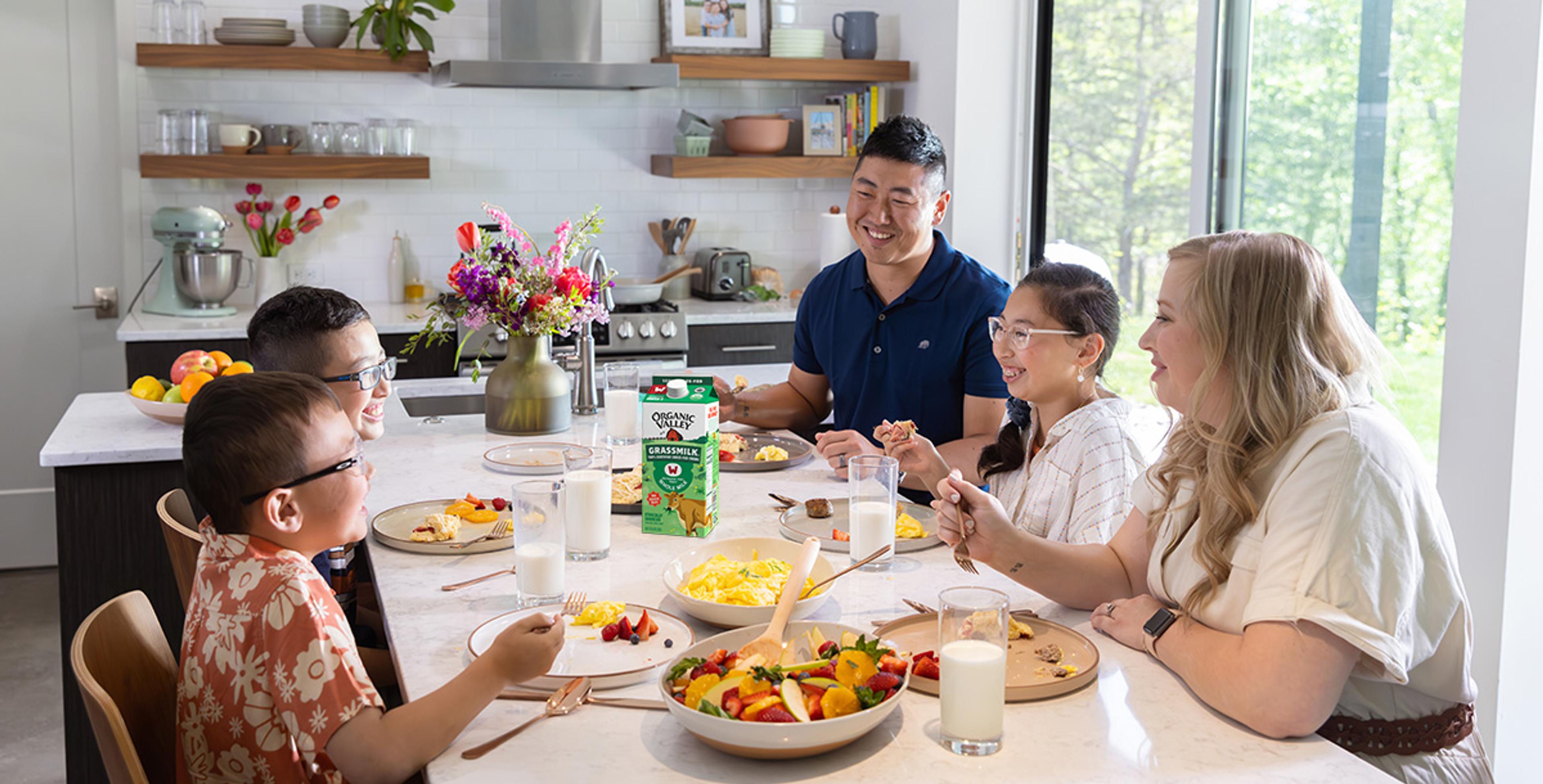 A family sitting around a table eating a meal with Grassmilk Whole Milk in the center.