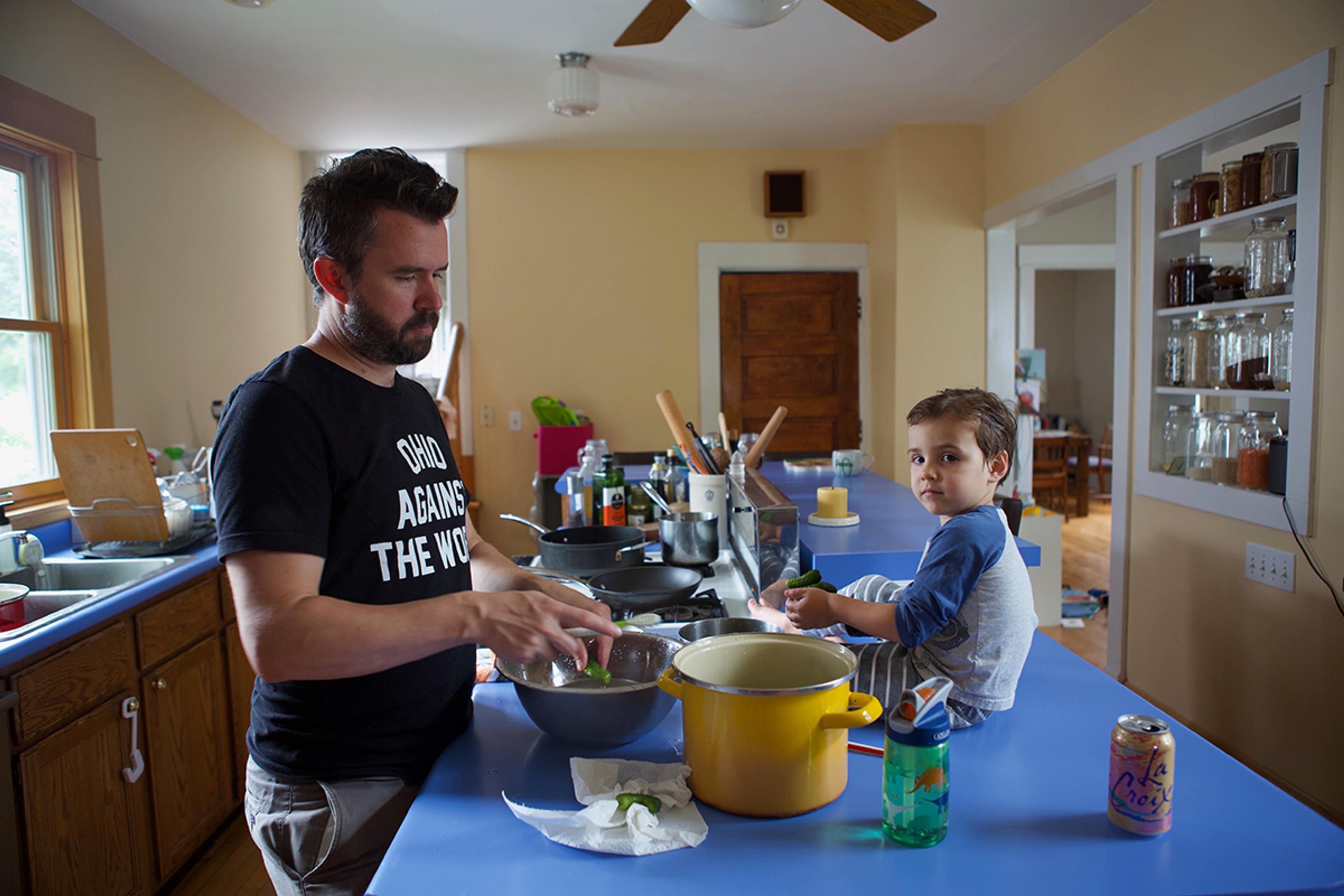 Dad making dinner with kid sitting on counter. Photo by The Perennial Plate.