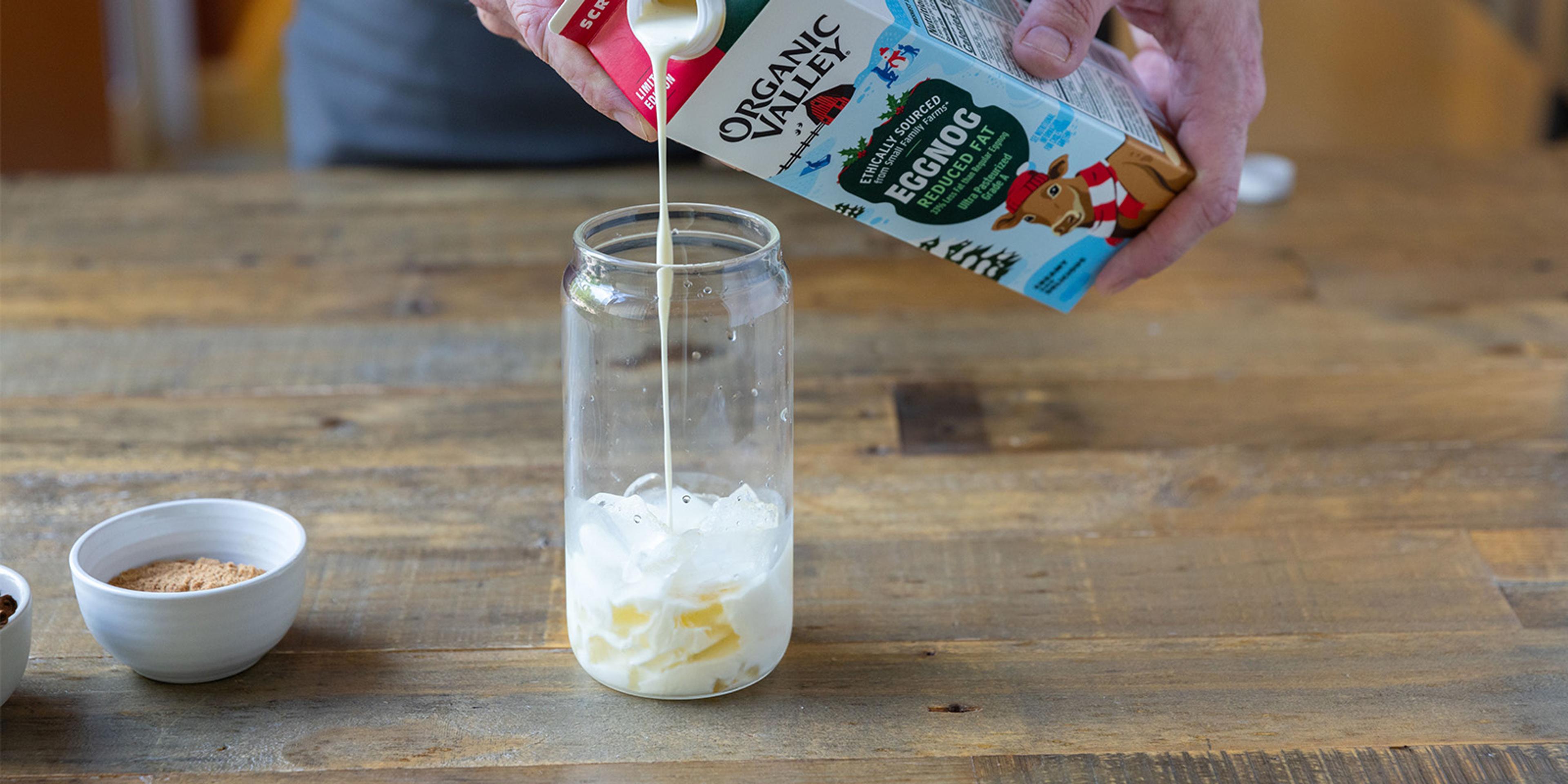 Eggnog is poured into a glass over ice.