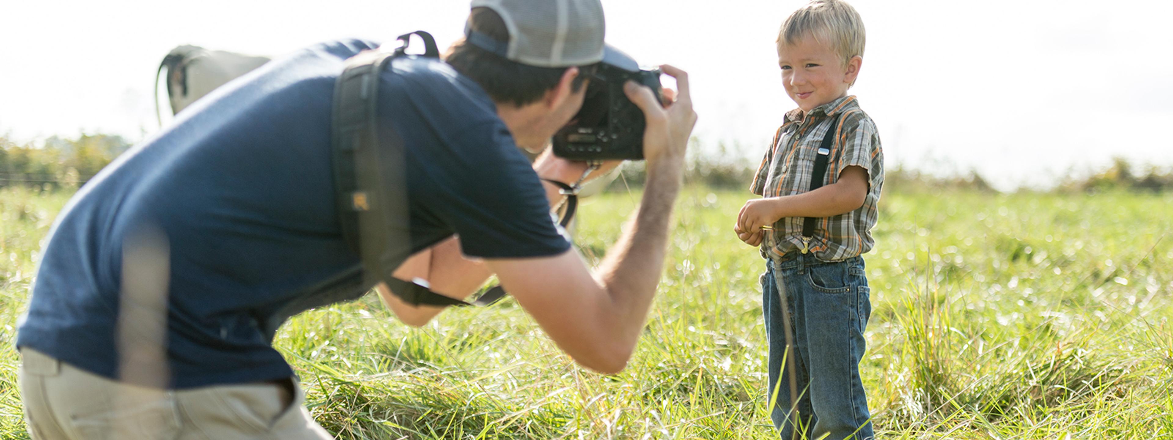 Man photographing young boy on a farm.