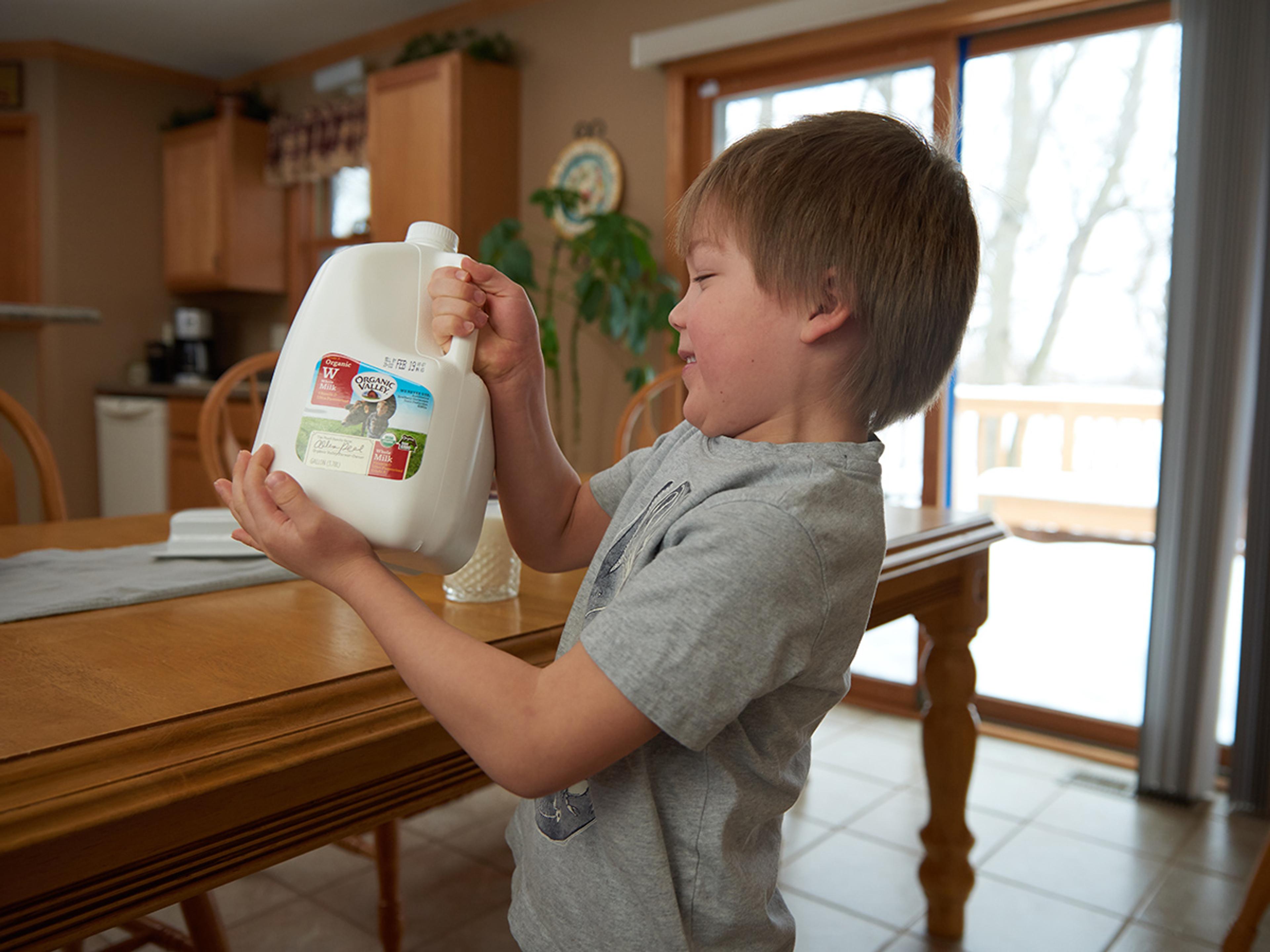A boy holds a gallon of Organic Valley milk and brings it to the table.