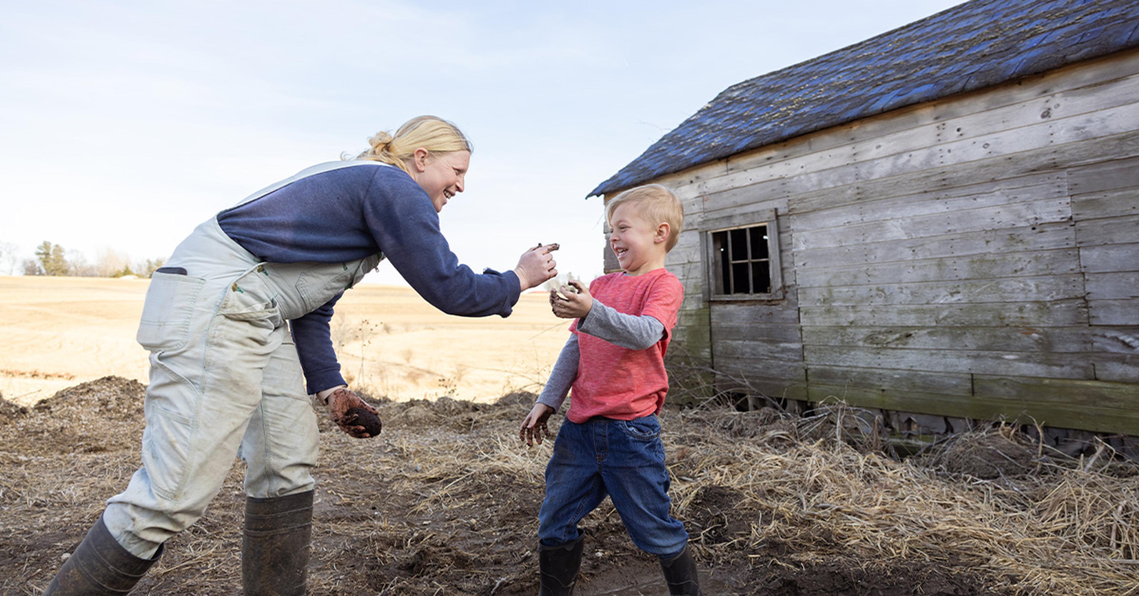 A mom attempts to wipe mud on her son’s face as he laughs.