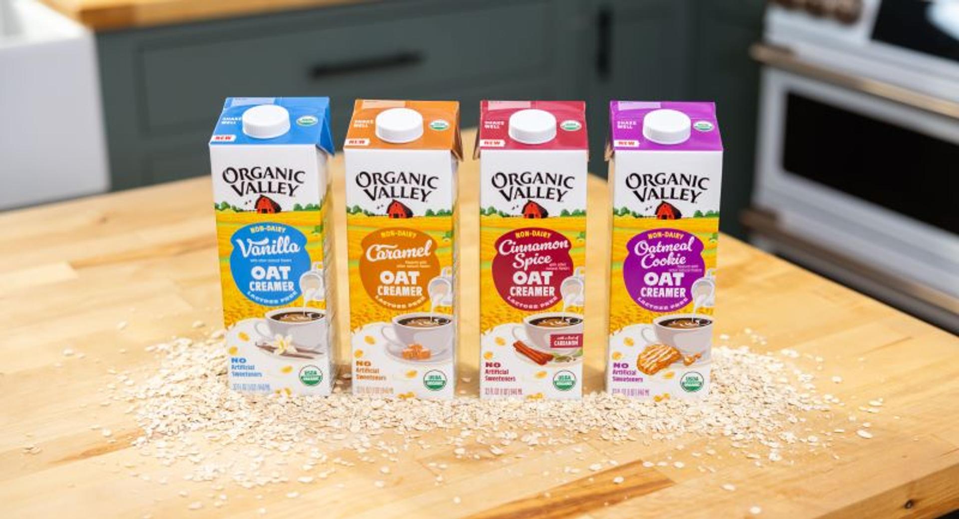 Cartons of organic oat creamers on a counter with oat scattered around.