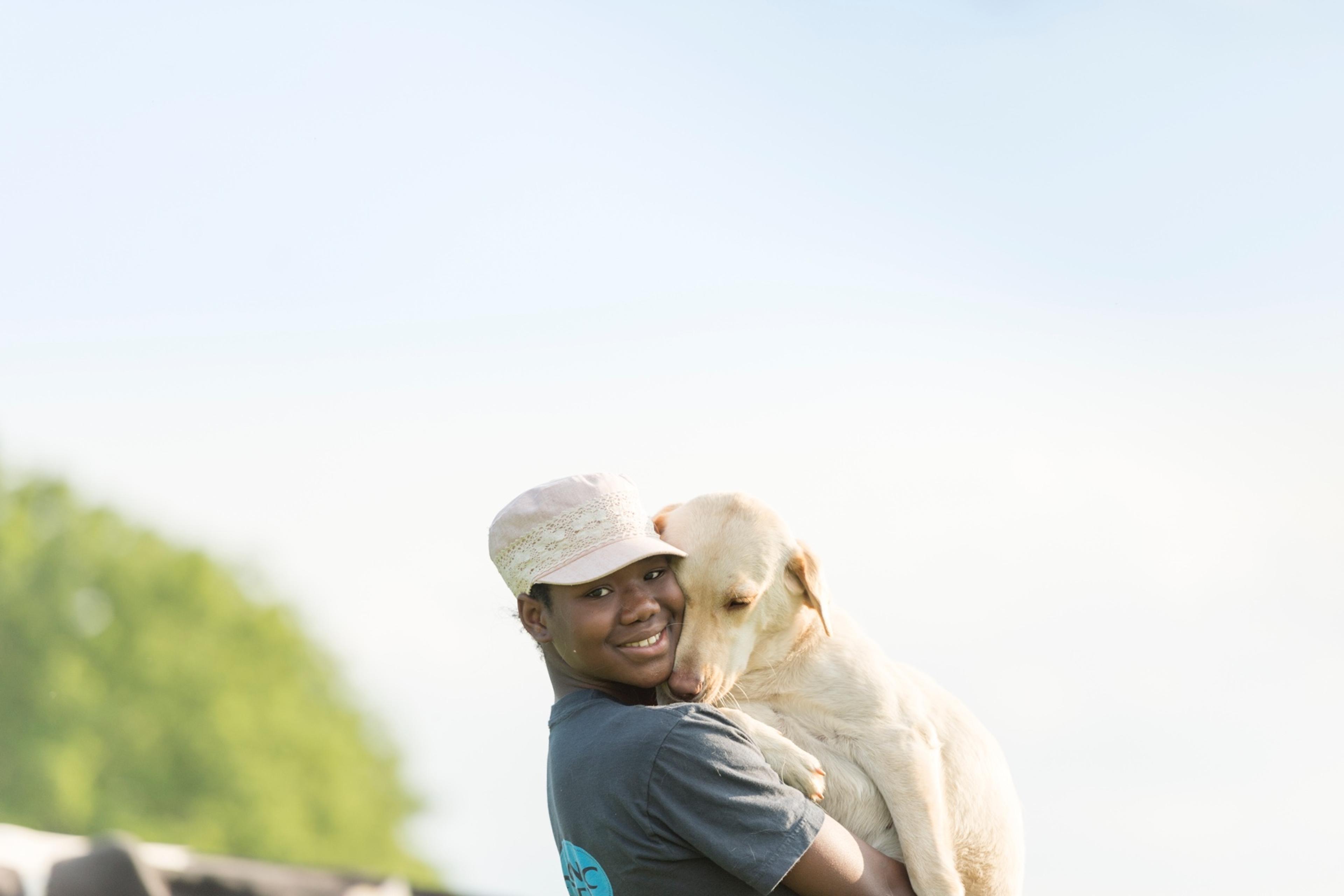 A woman smiles at the camera while holding her yellow lab, which lovingly snuggles into her neck.