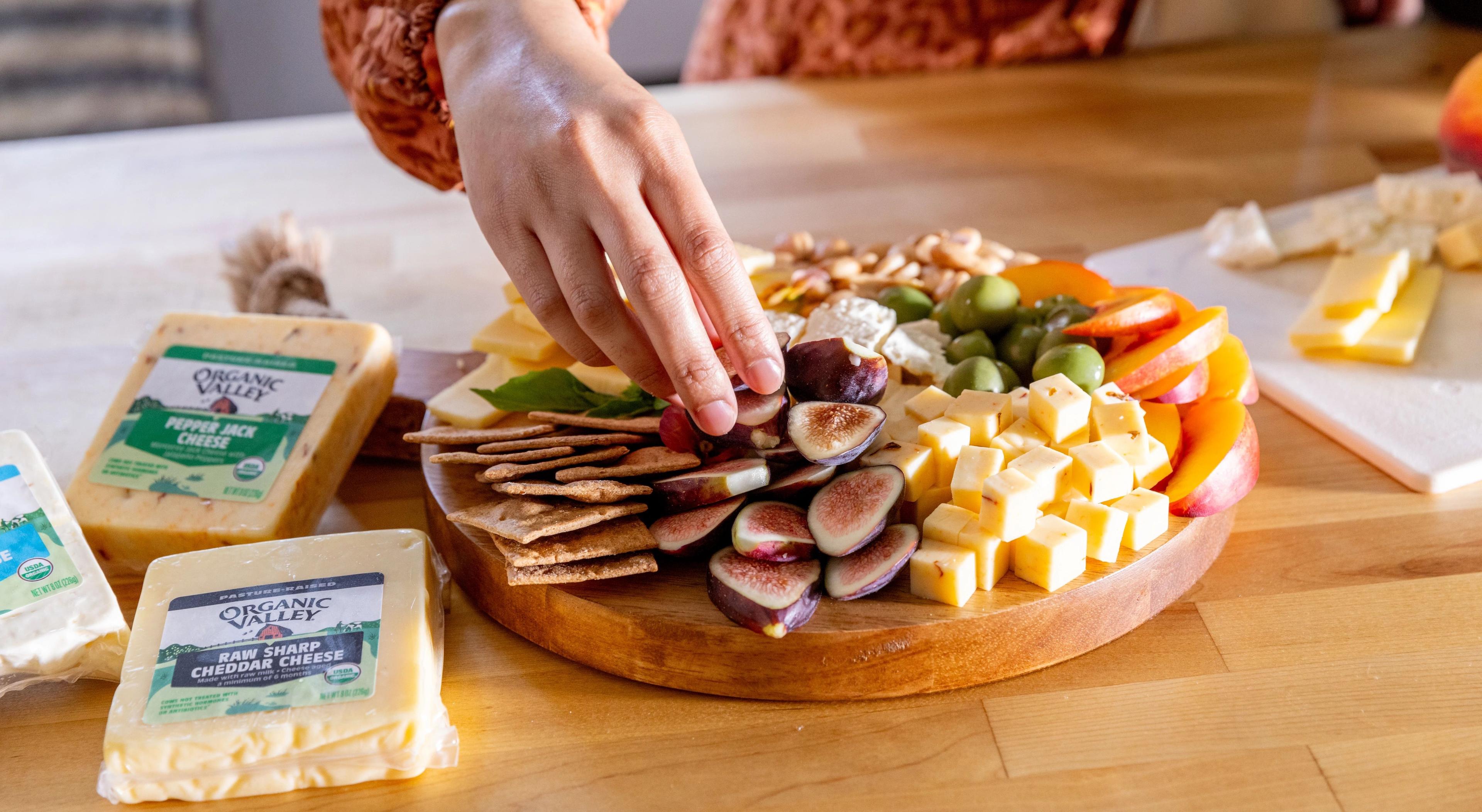 A woman arranges cheese, crackers, olives on a board.