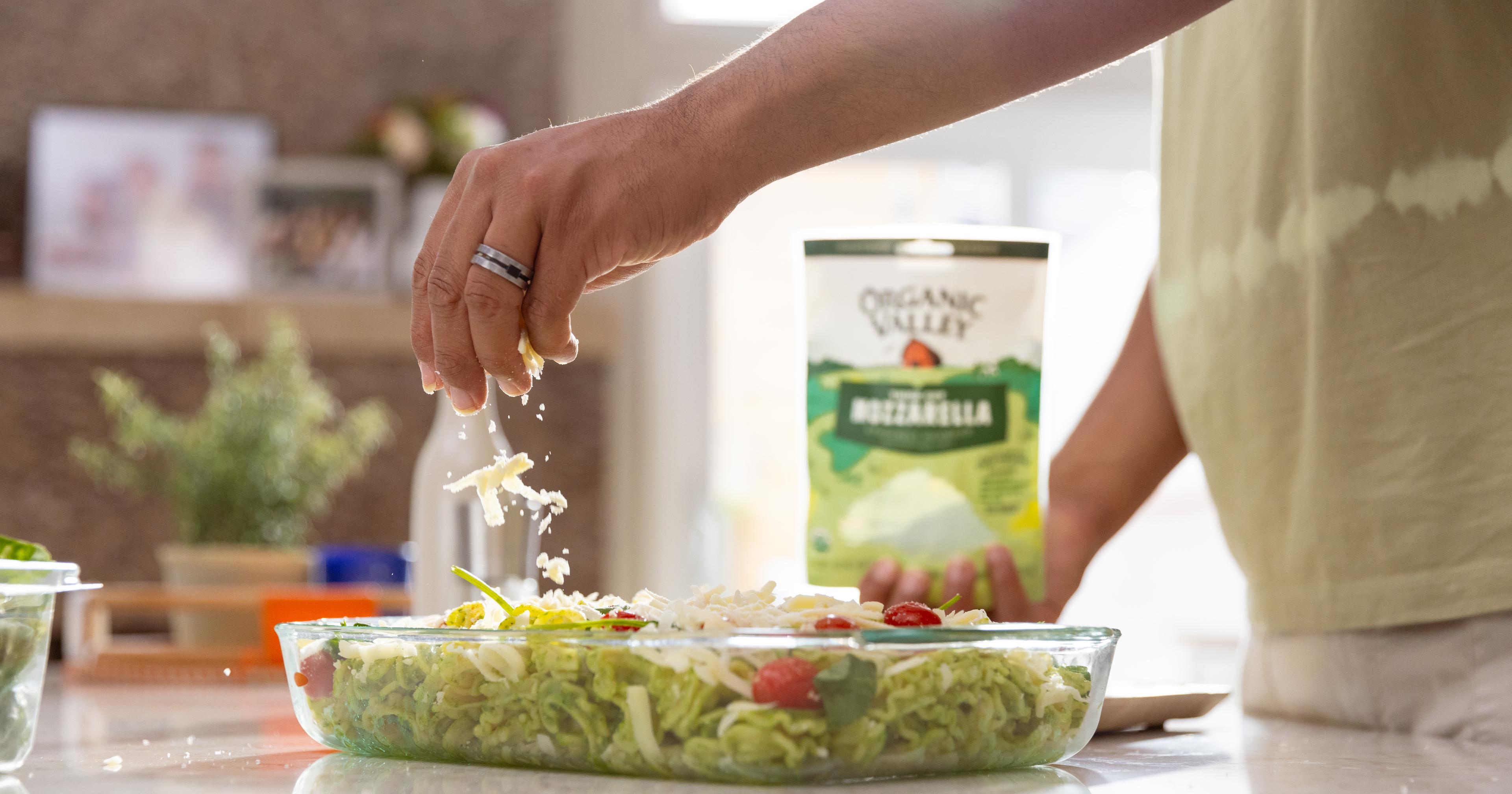 A man sprinkles organic mozzarella cheese on a dish.