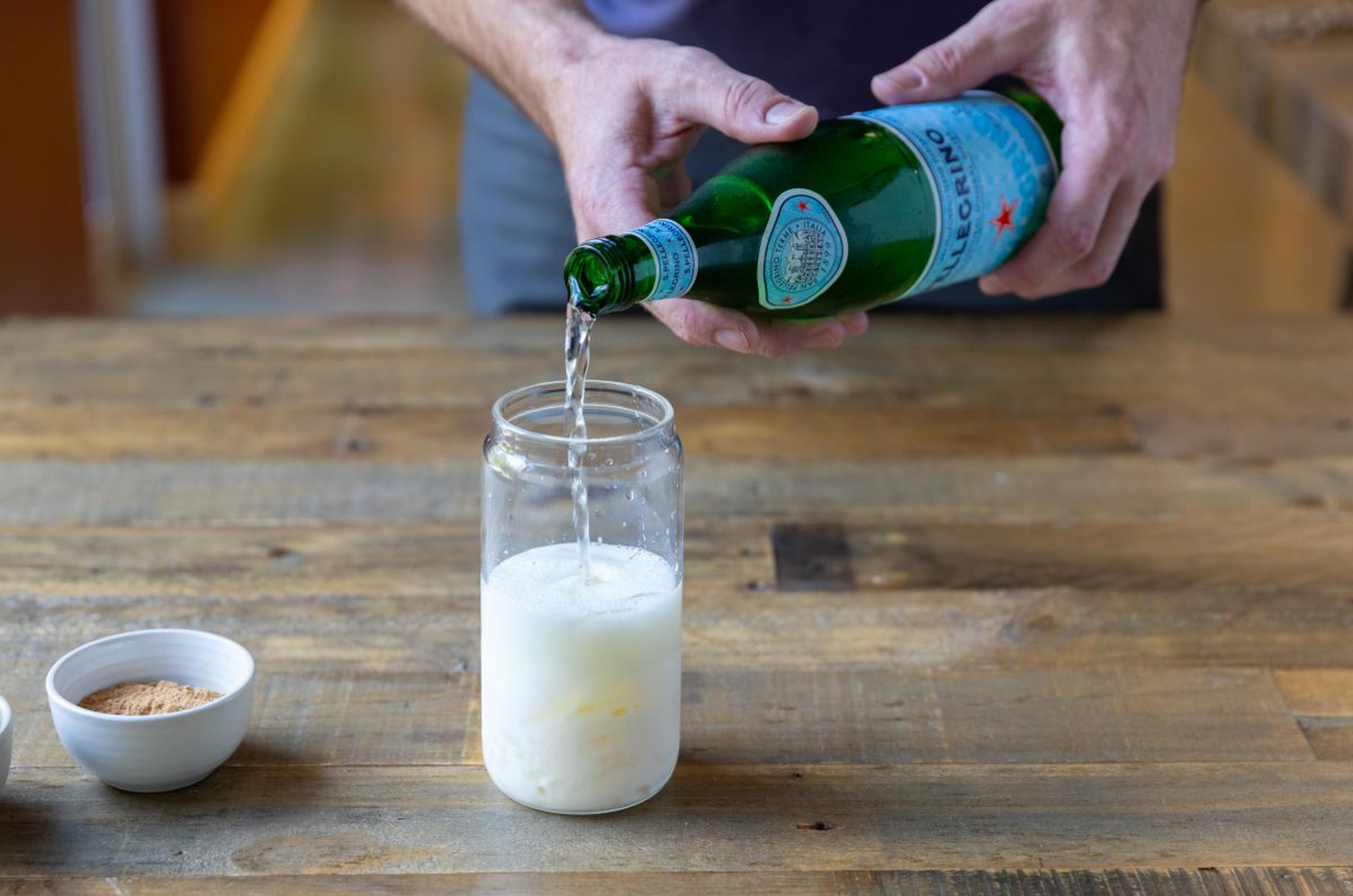 Eggnog is poured into a glass over ice.