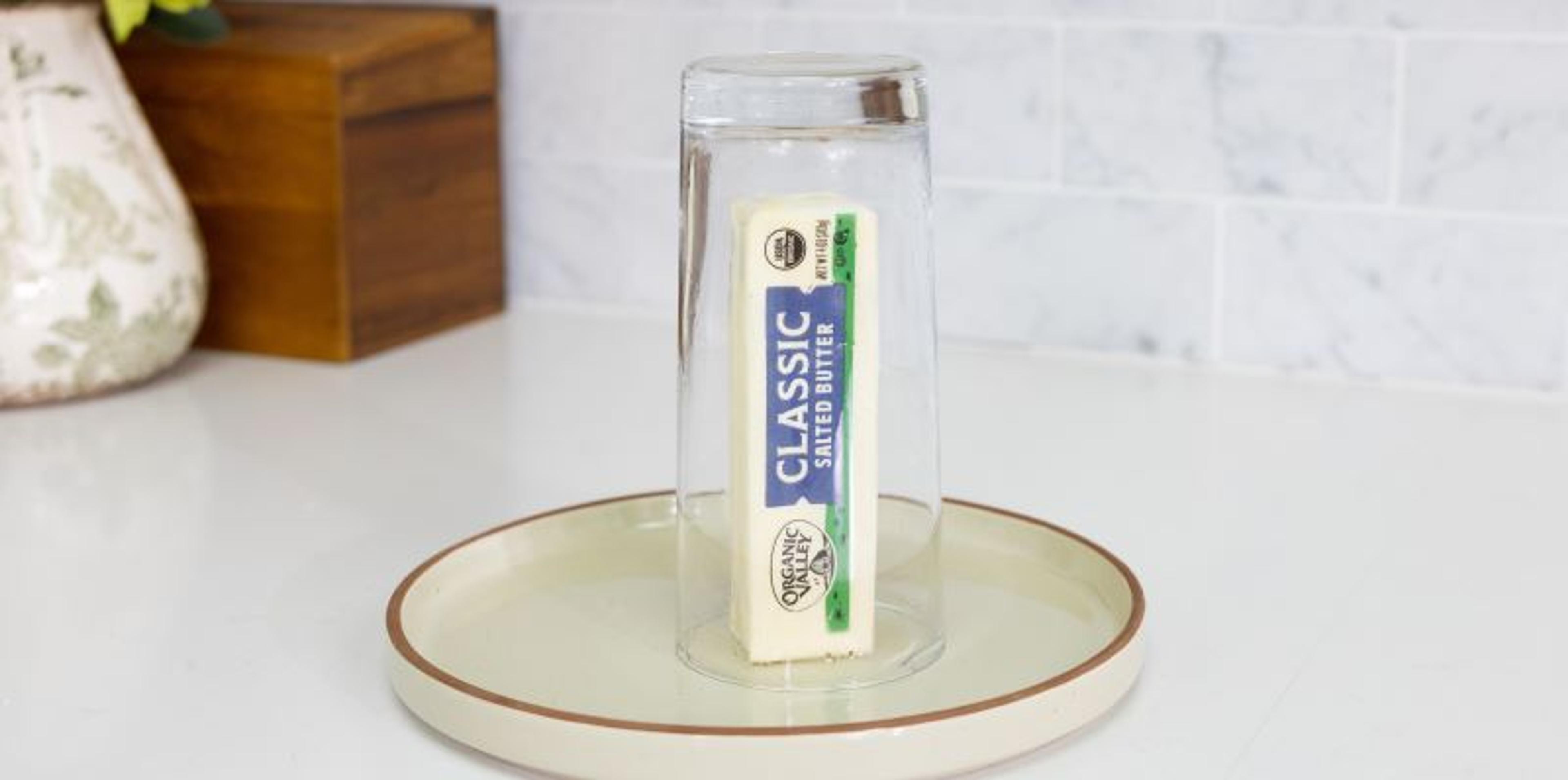 A stick of butter on a plate with a glass over it.