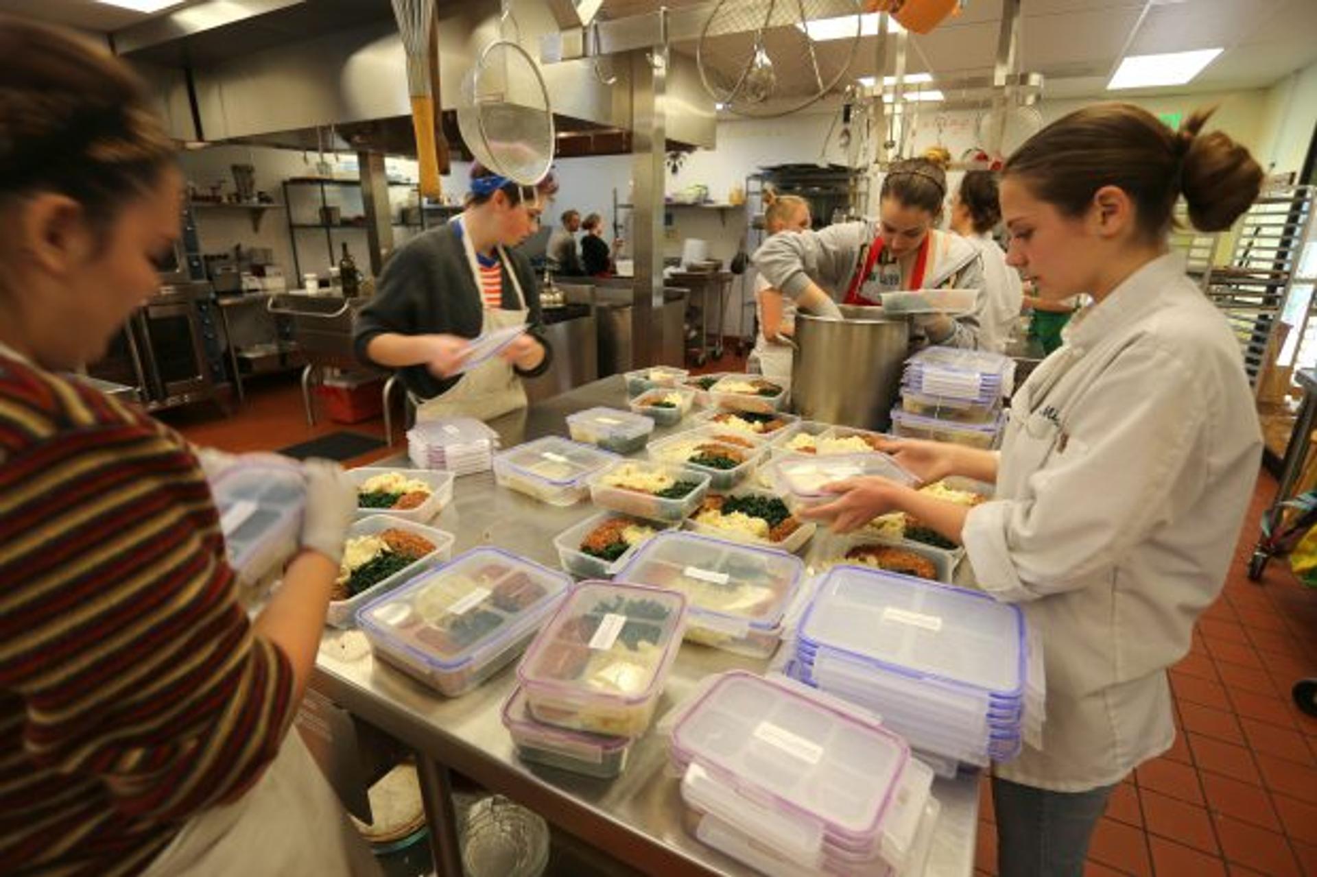 Teen chefs fill meal containers for the day's deliveries of nutritious food.