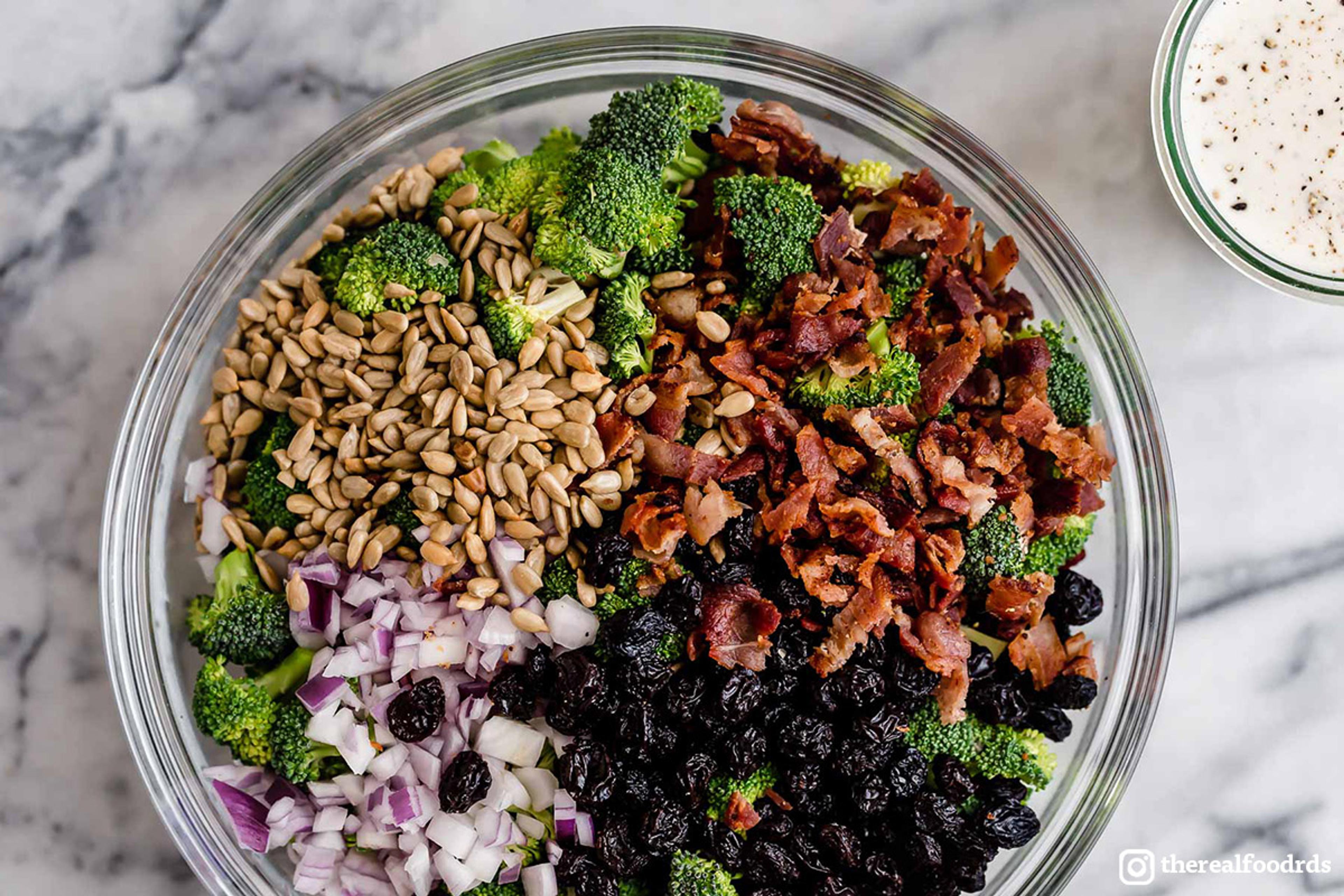Ingredients for a healthy broccoli salad in a bowl viewed from above on a marble countertop.