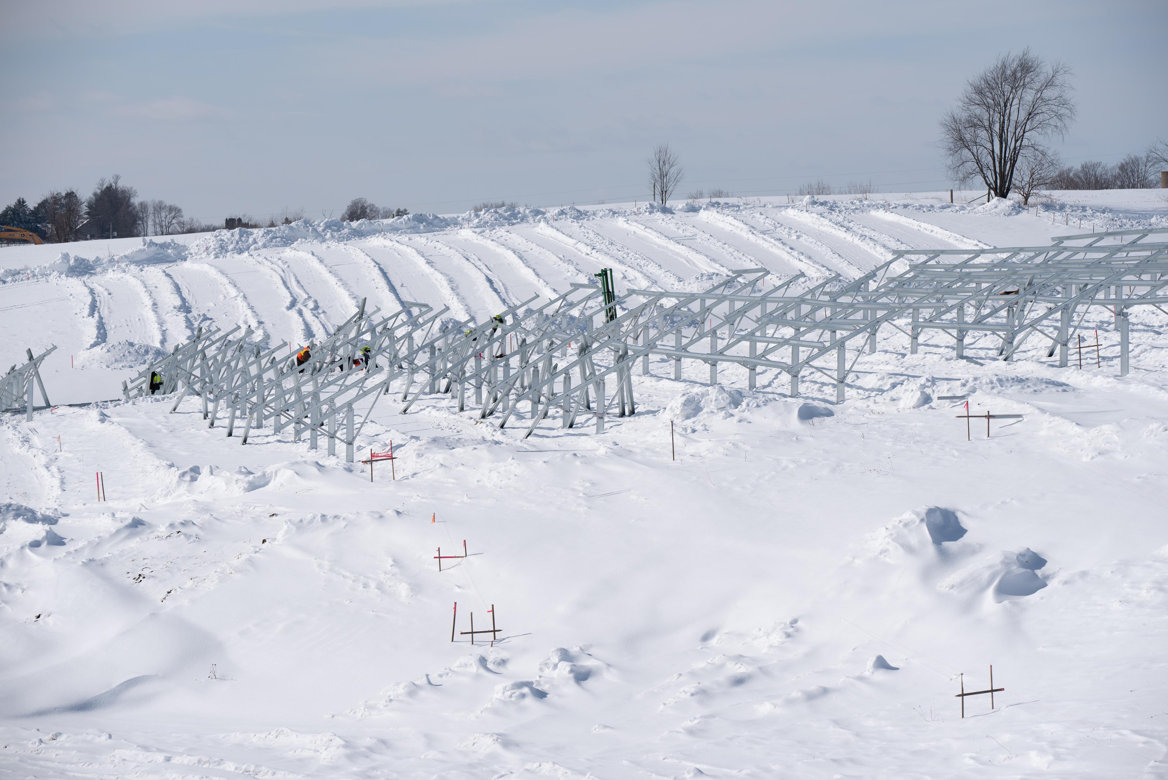 Workers installing the supports for solar panels in a snow-covered field.