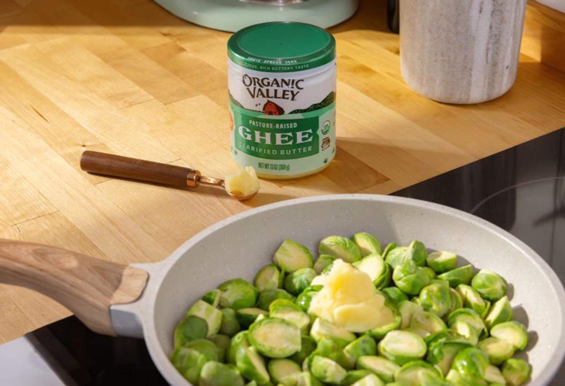 A jar of ghee next to a pan of Brussels sprouts.