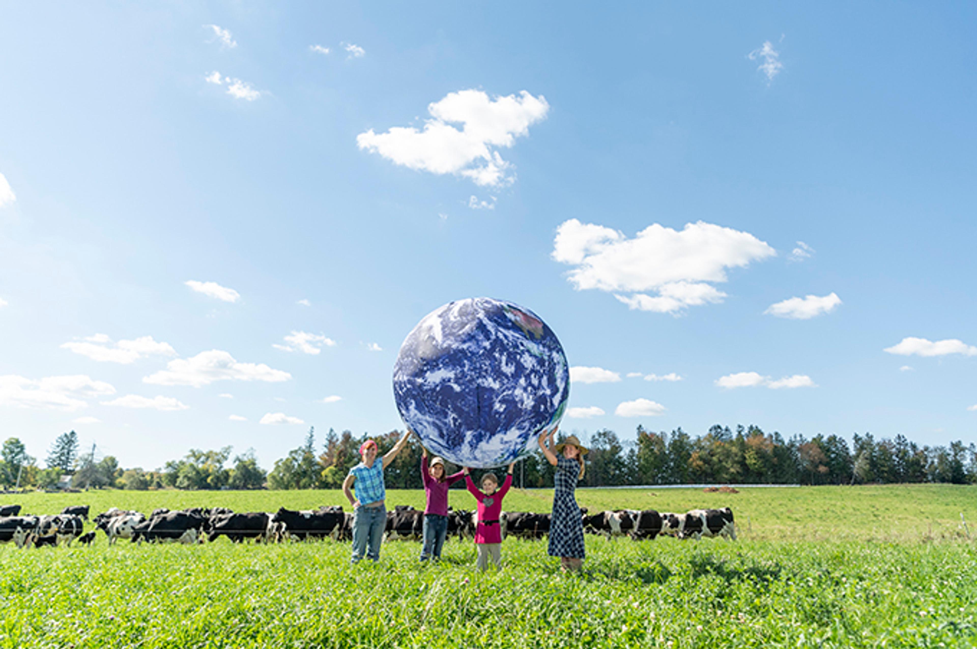 Farmers and family holding a large earth in a cow pasture surounded by cows.
