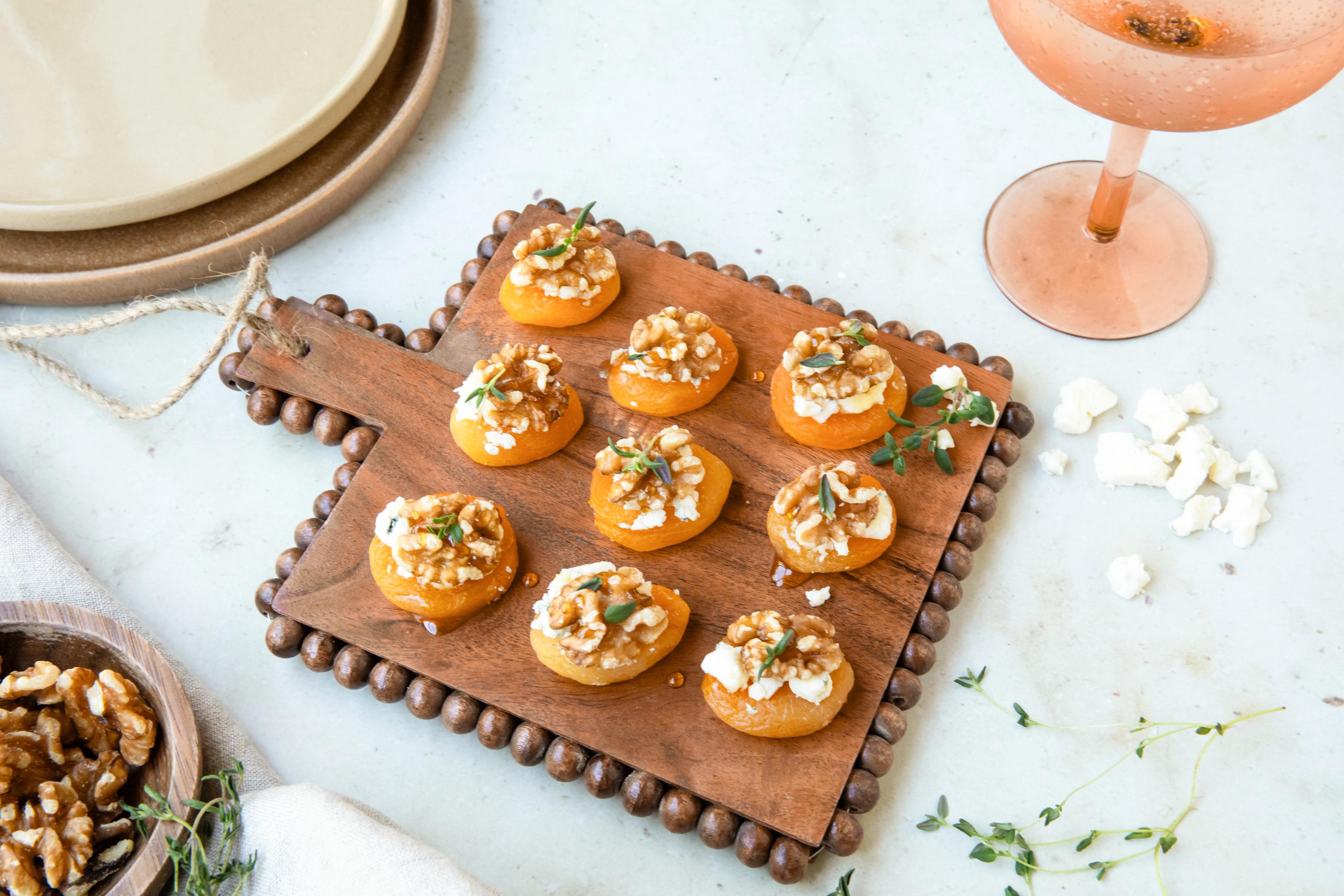 A festive finger food, blue cheese stuffed apricots, on a counter next to a martini glass.