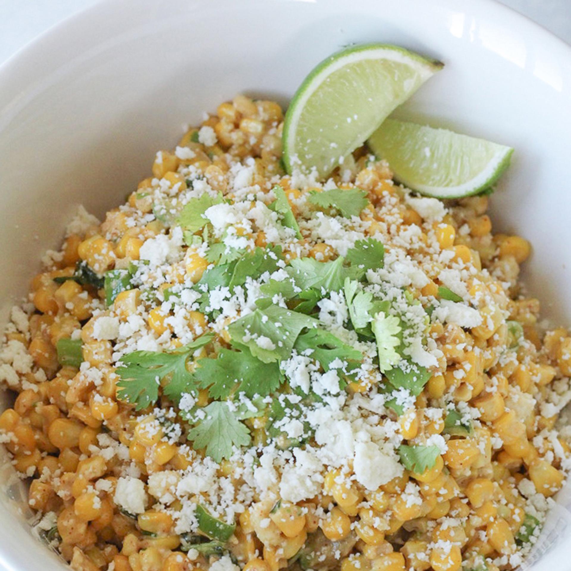 Fresh sweet corn off the cob made into a Mexican corn salad topped with fresh cheese cilantro and lime wedges.