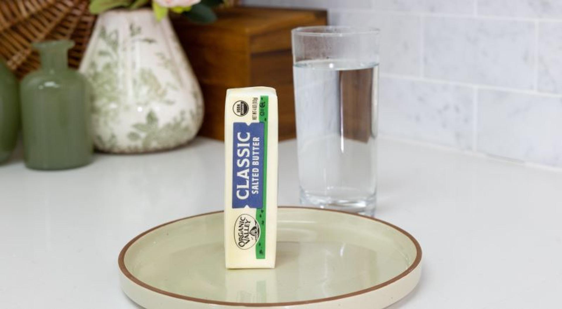 A stick of butter next to a glass of water.
