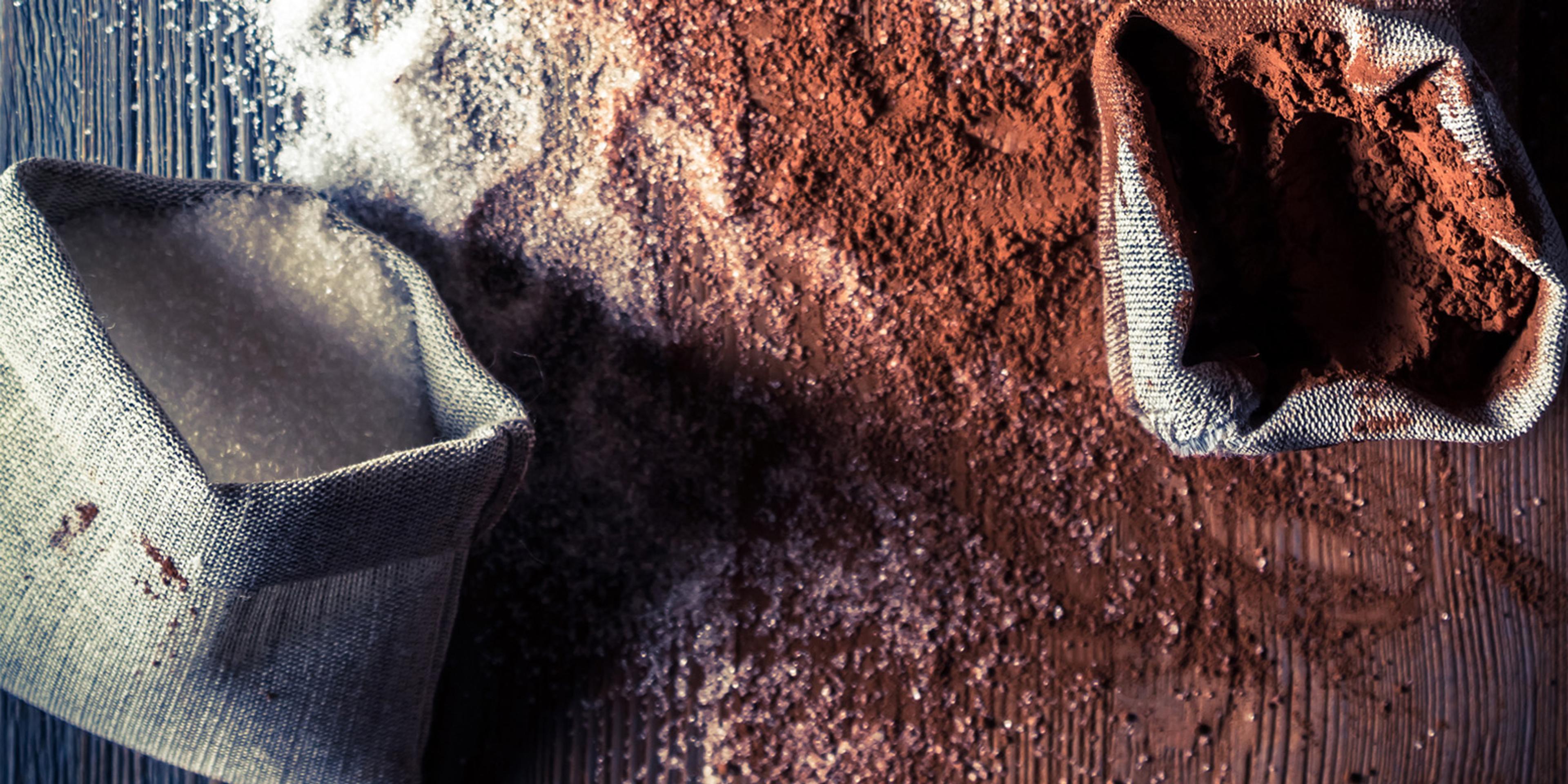 Overhead view cocoa powder and cane sugar spread across a wooden counter.
