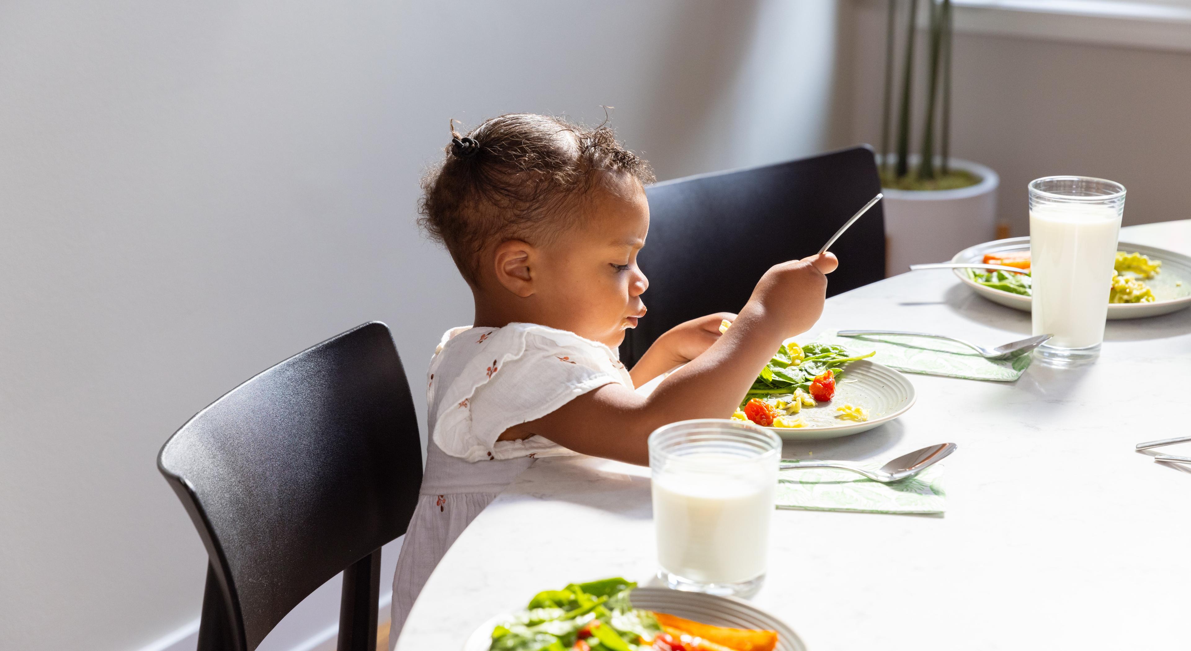Milk is on the table as a toddler eats.