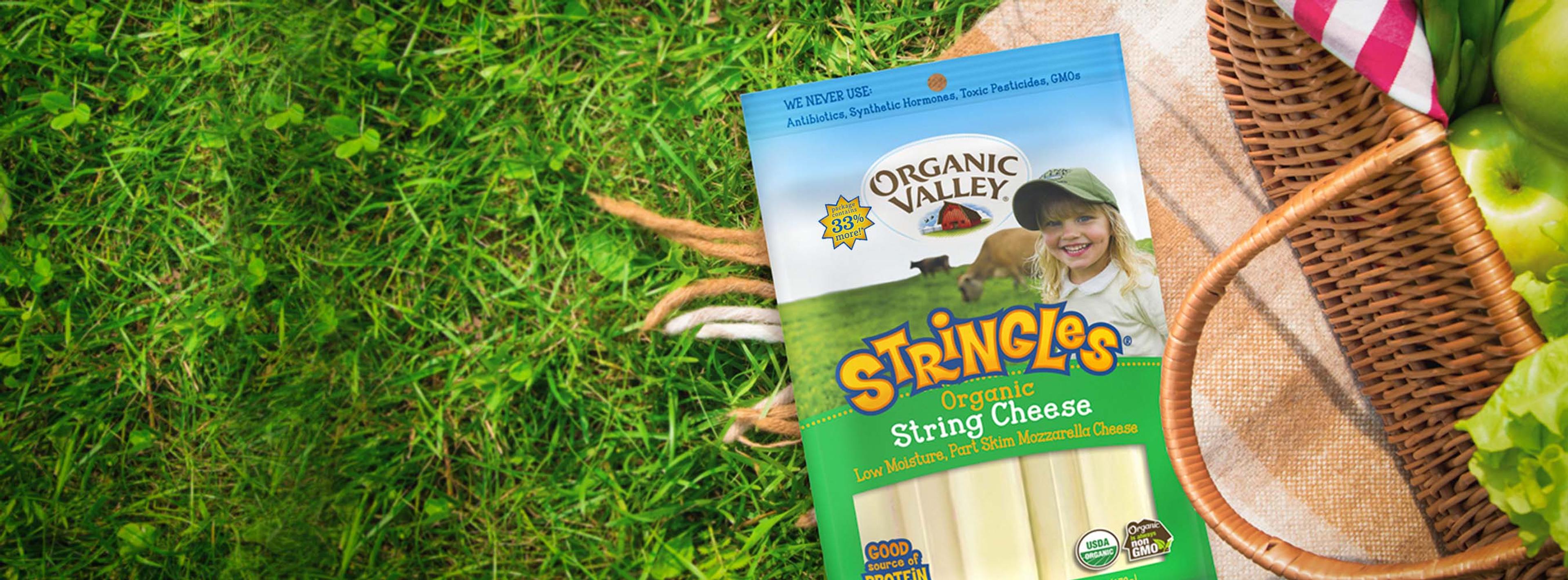 A package of Stringles next to a picnic basket on the grass. 