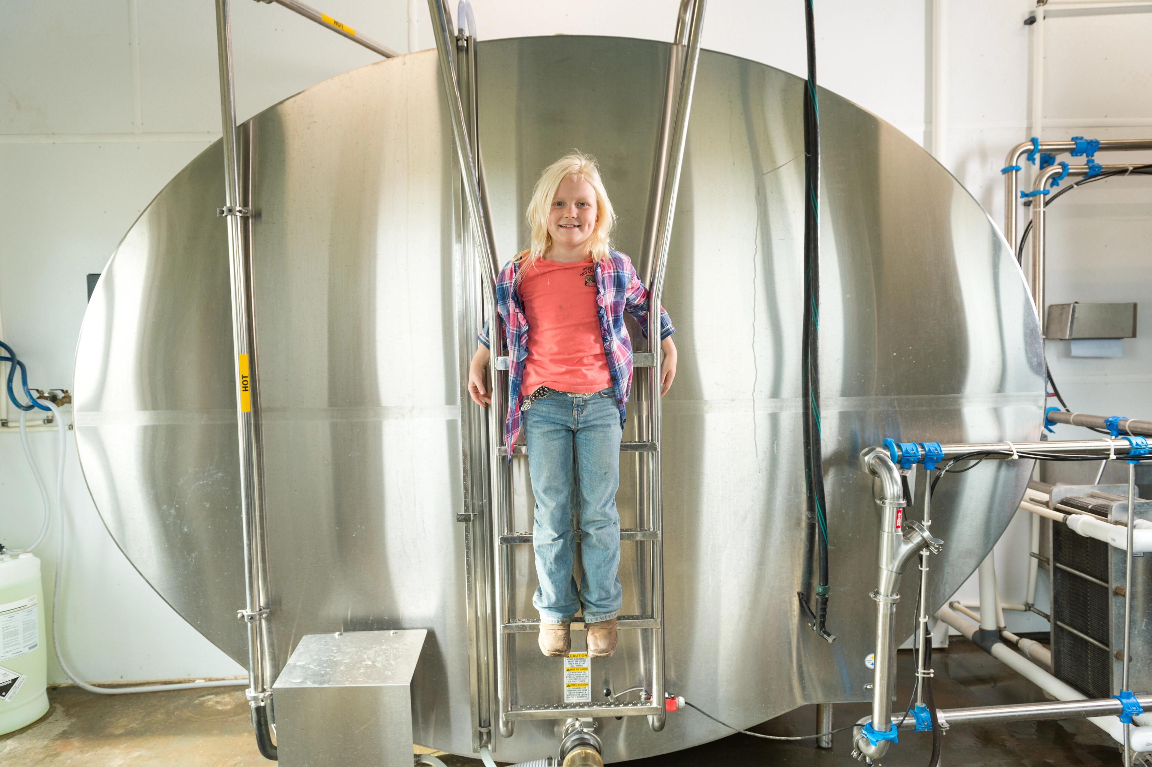 A girl stands on a ladder attached to the big, silver bulk tank that holds fresh milk at the Perkins family farm in West Virginia. 