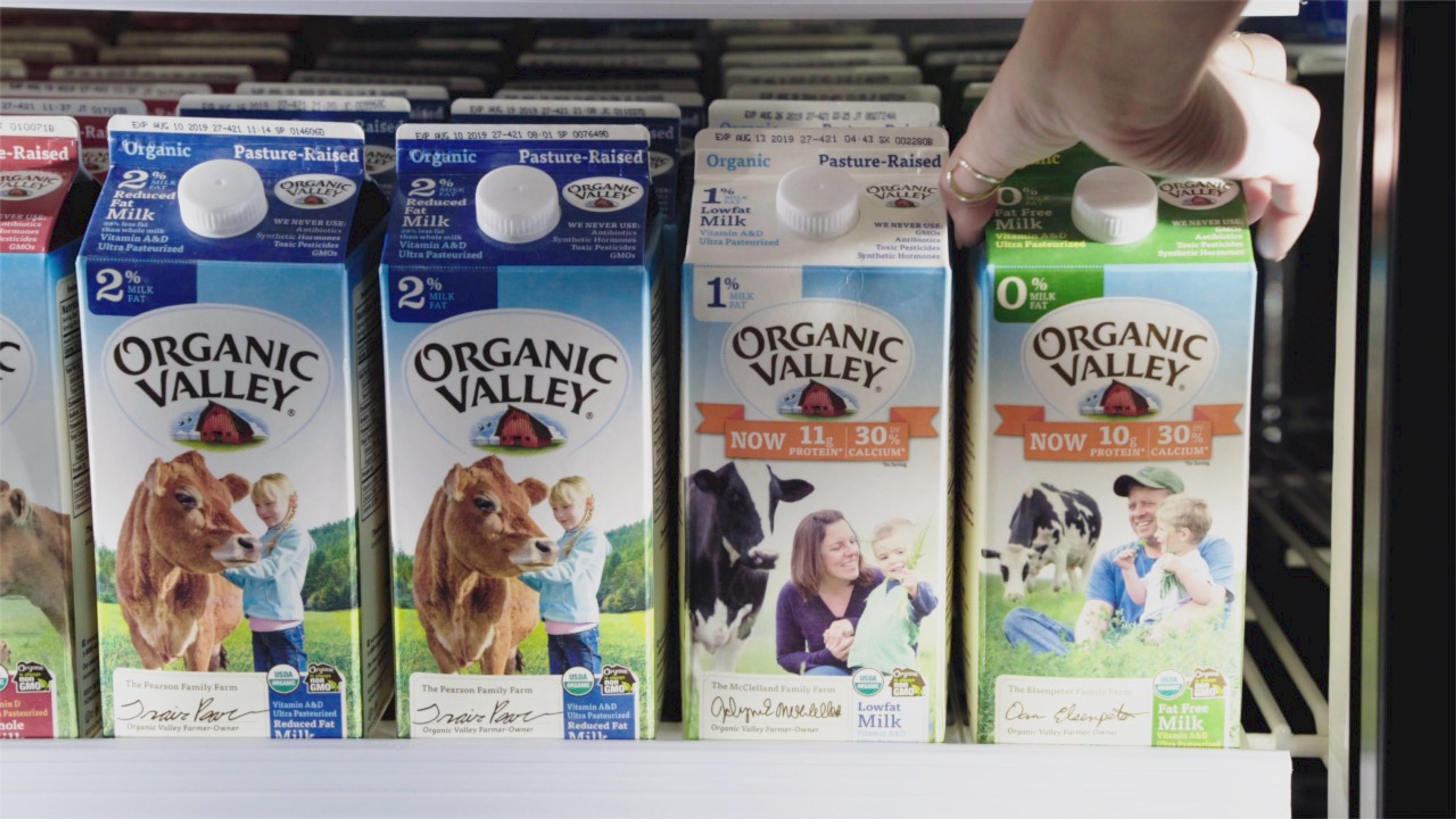 A hand reaches for a carton of Organic Valley Fortified Milk in the dairy case at a grocery store.