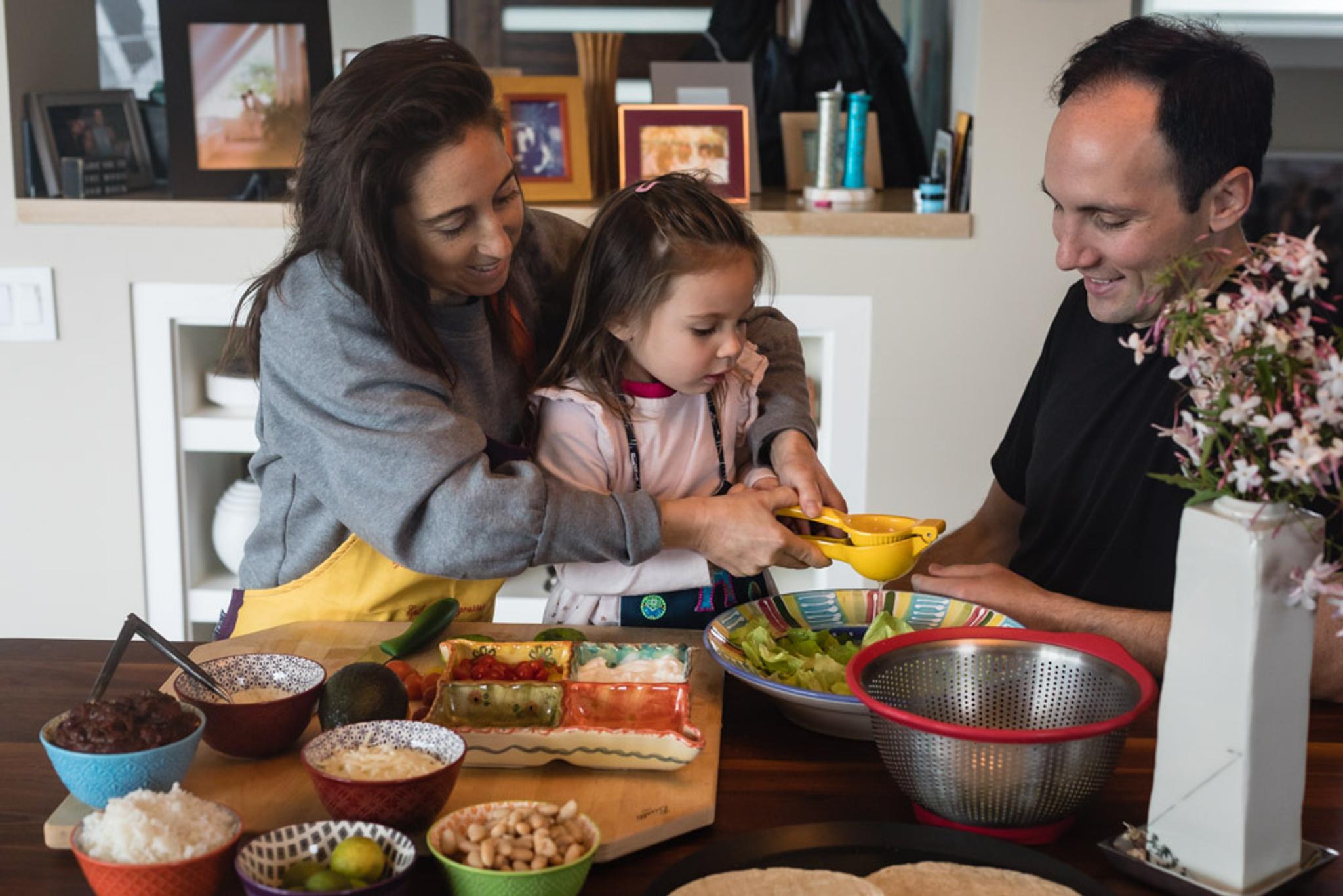 A mother, father and daughter prepare a taco spread together.