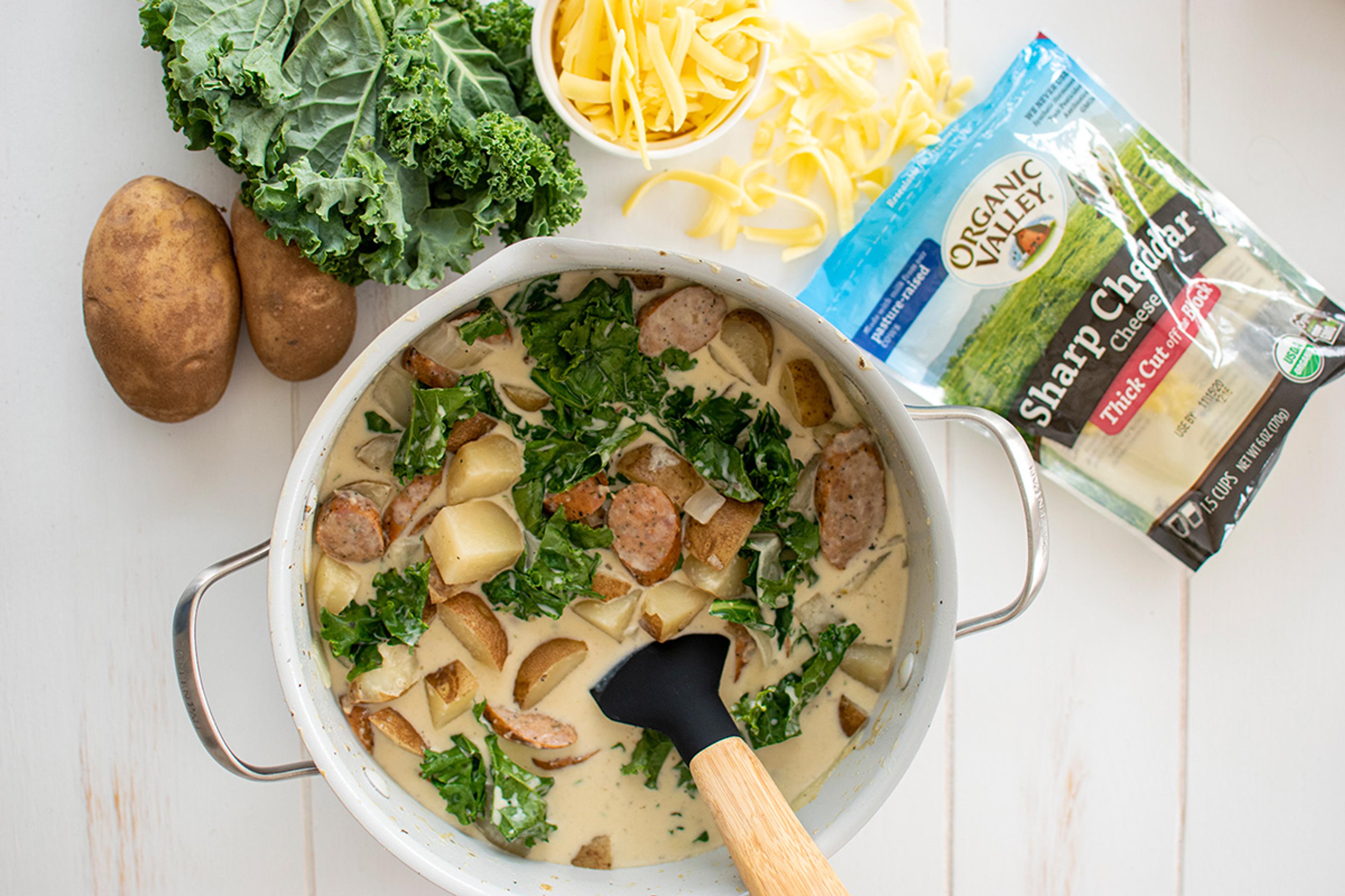 Creamy sausage potato and kale soup with thick-cut sausage, potato chunks, and wilted kale topped with shredded cheese.