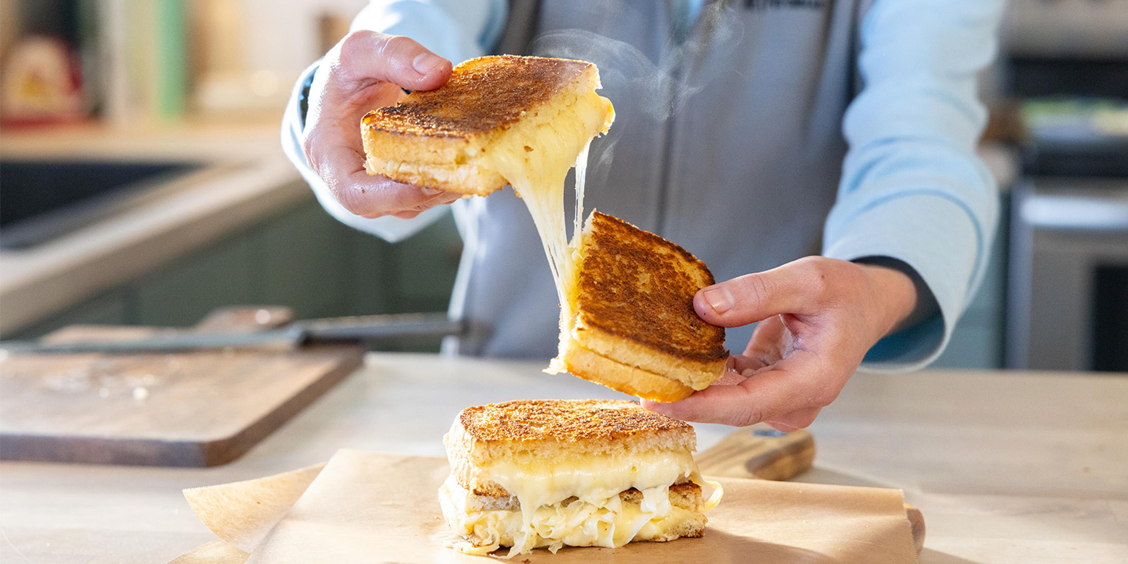 A person holds a gooey grilled cheese sandwich.