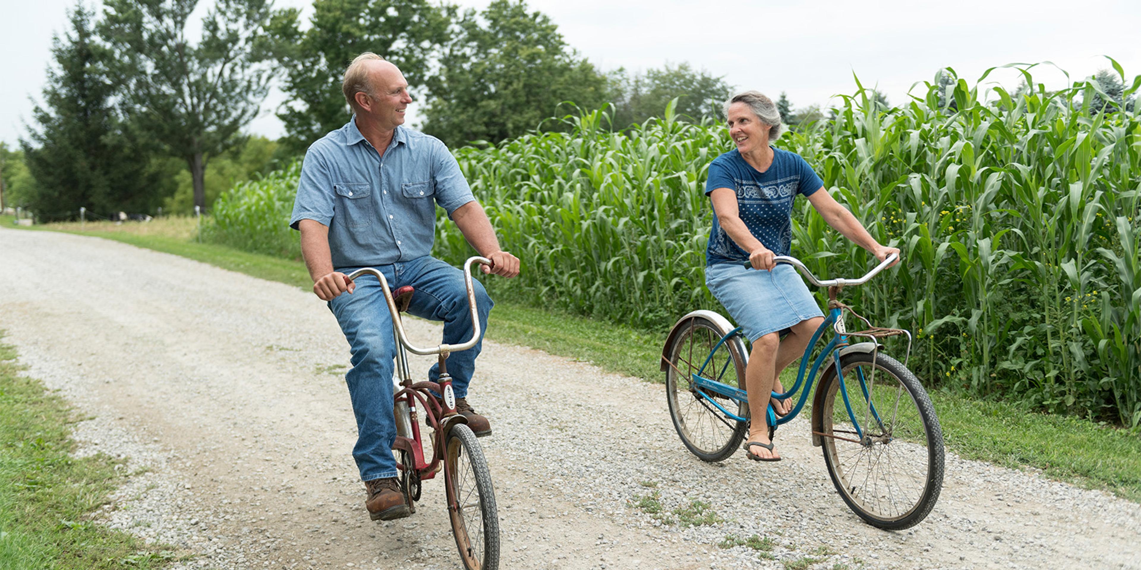 Jim and Janice Gasser ride bikes by a field of corn on their organic dairy farm.