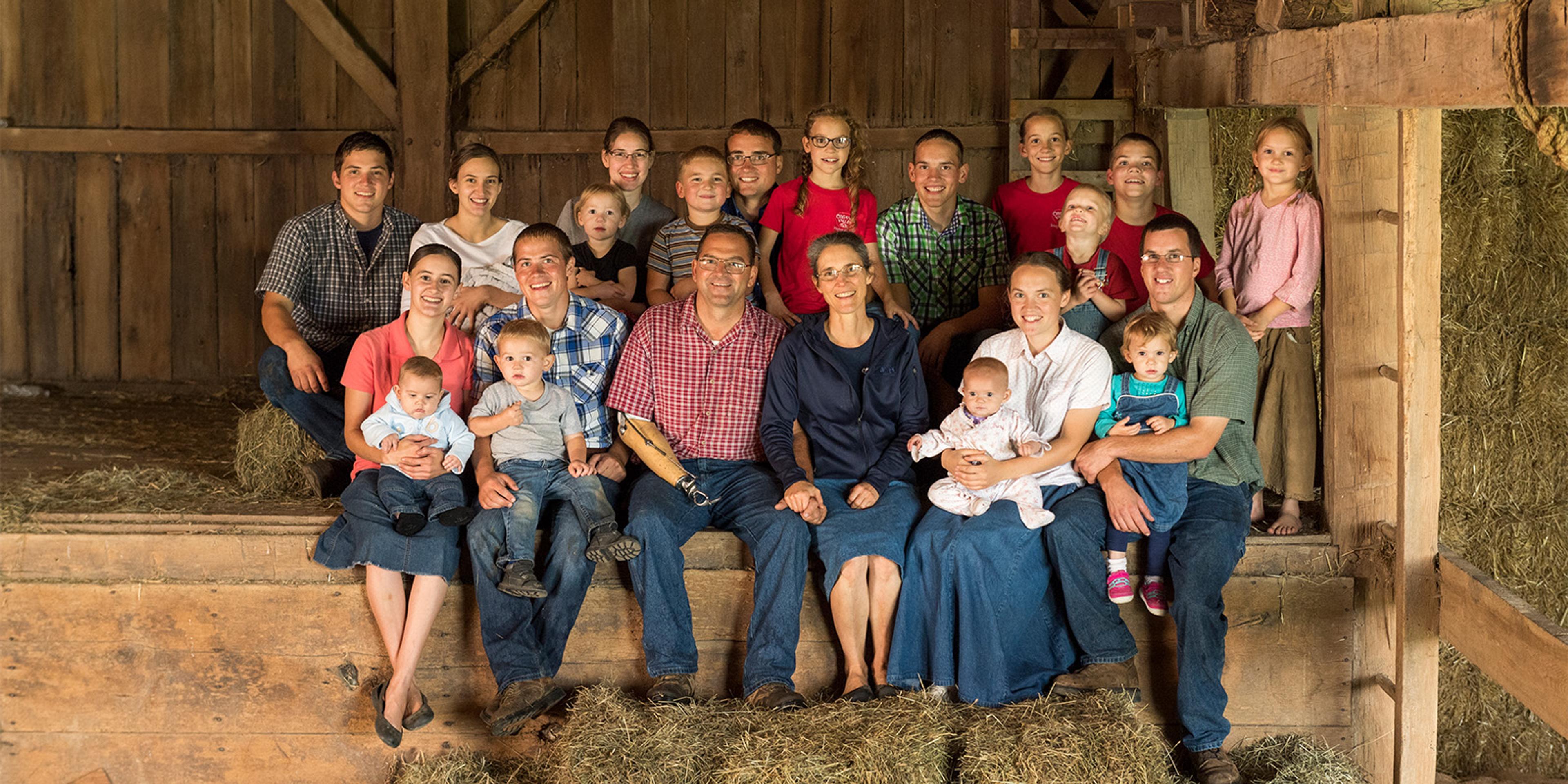 Members of the Stoller family sit in a barn near stacks of hay.