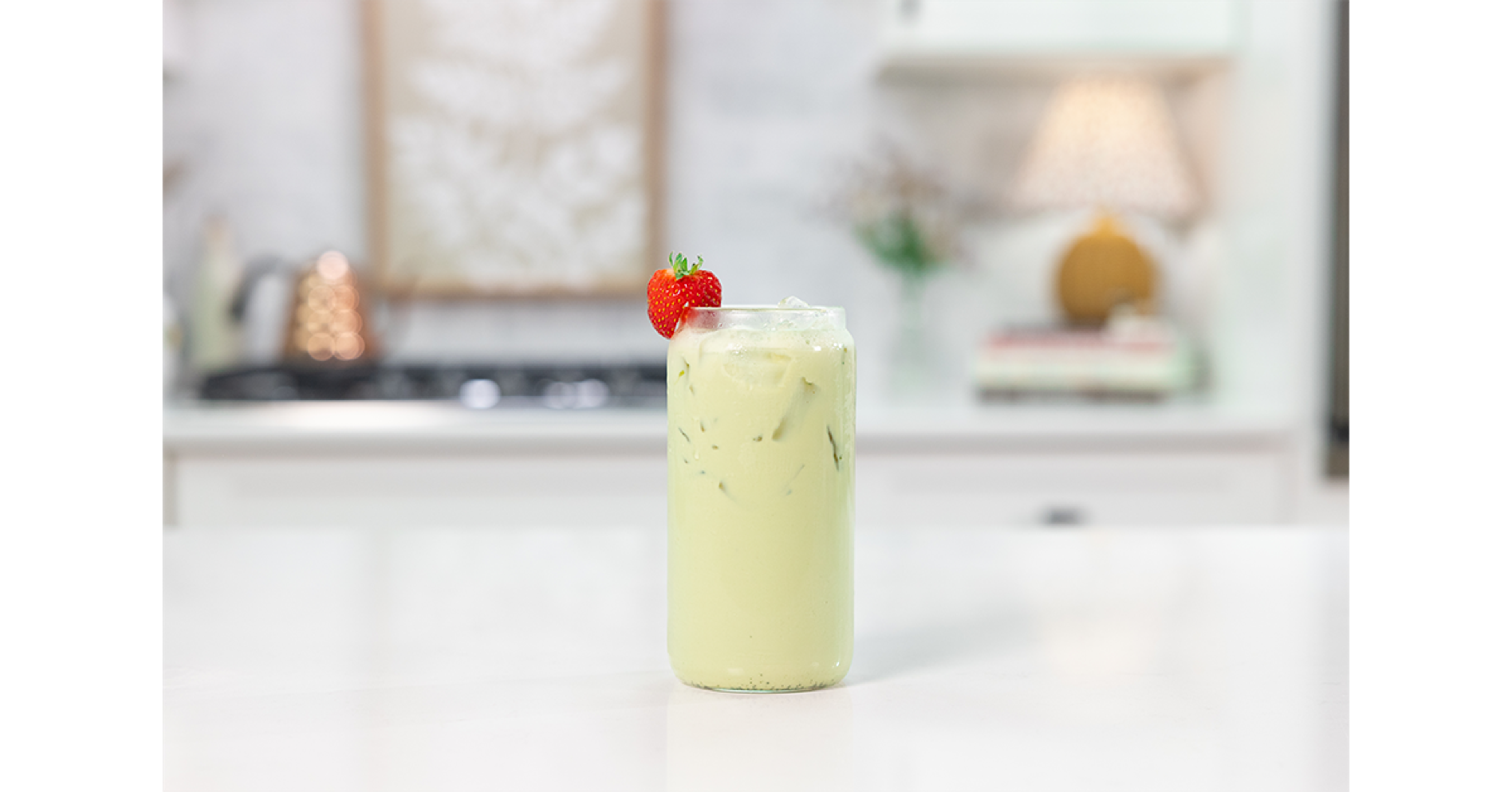 Strawberry Matcha with ice in a glass on a counter with a strawberry as a garnish.
