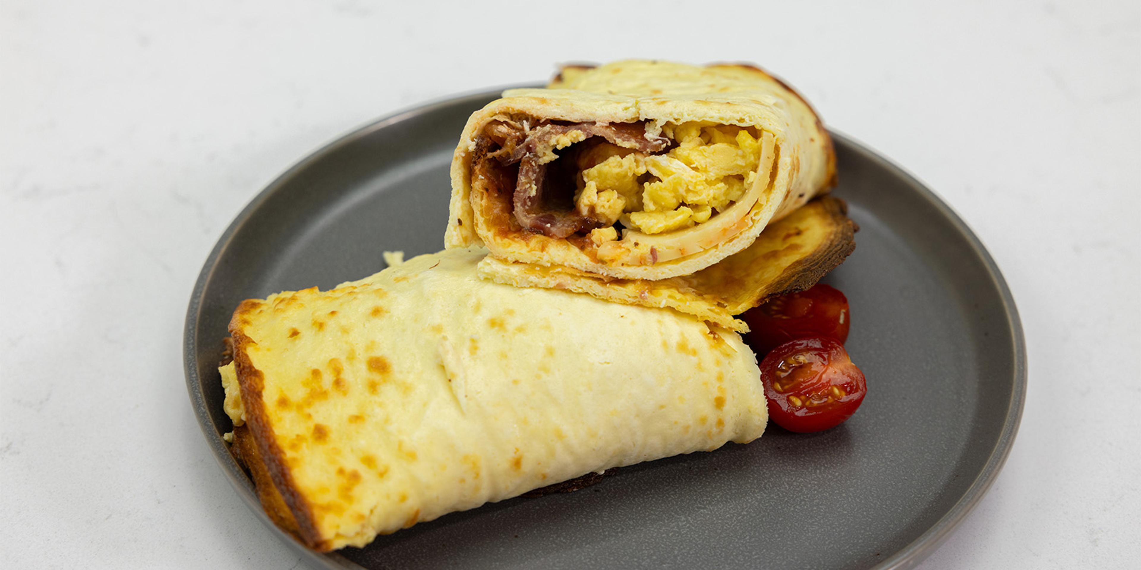 A cottage cheese breakfast wrap on a plate with tomatoes.