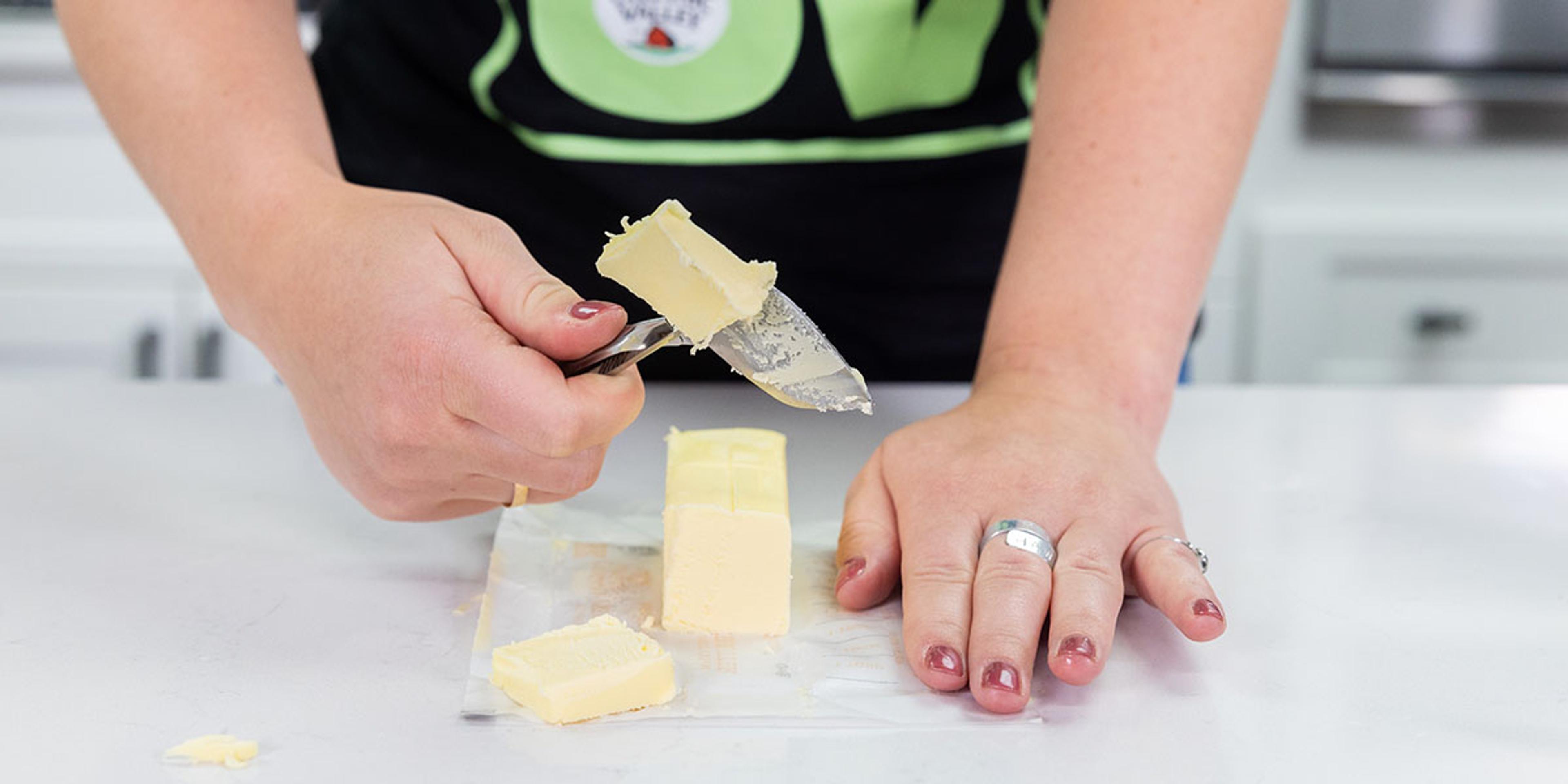A woman slices butter with a gadget.