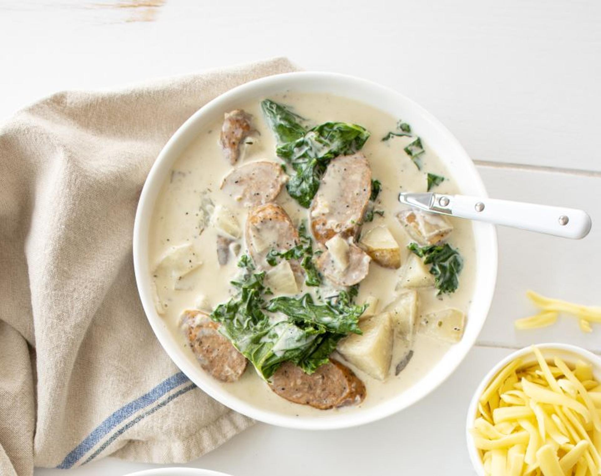 Creamy sausage potato and kale soup with thick-cut sausage, potato chunks, and wilted kale topped with shredded cheese.