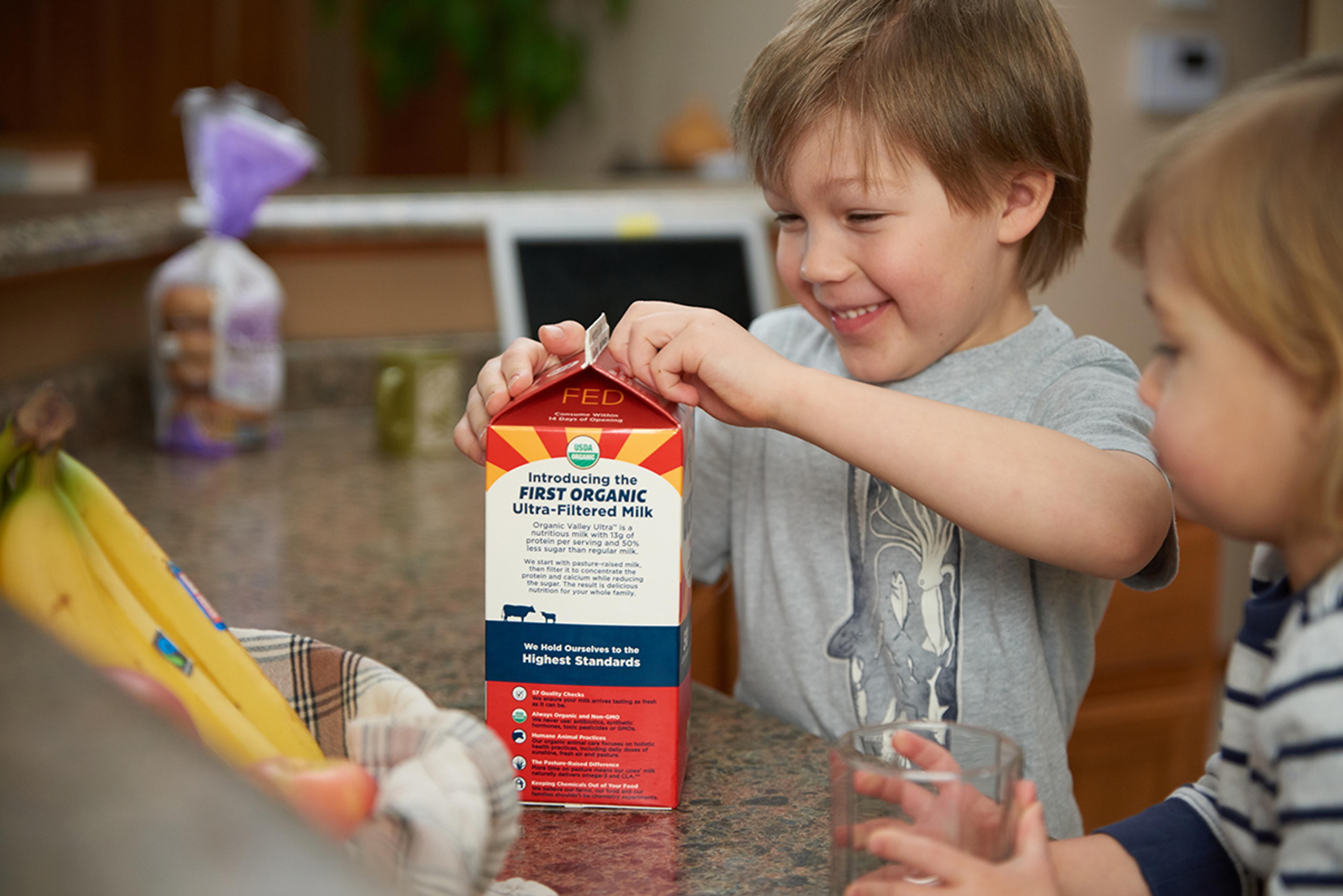Two young boys excitedly open a carton of milk on the counter.