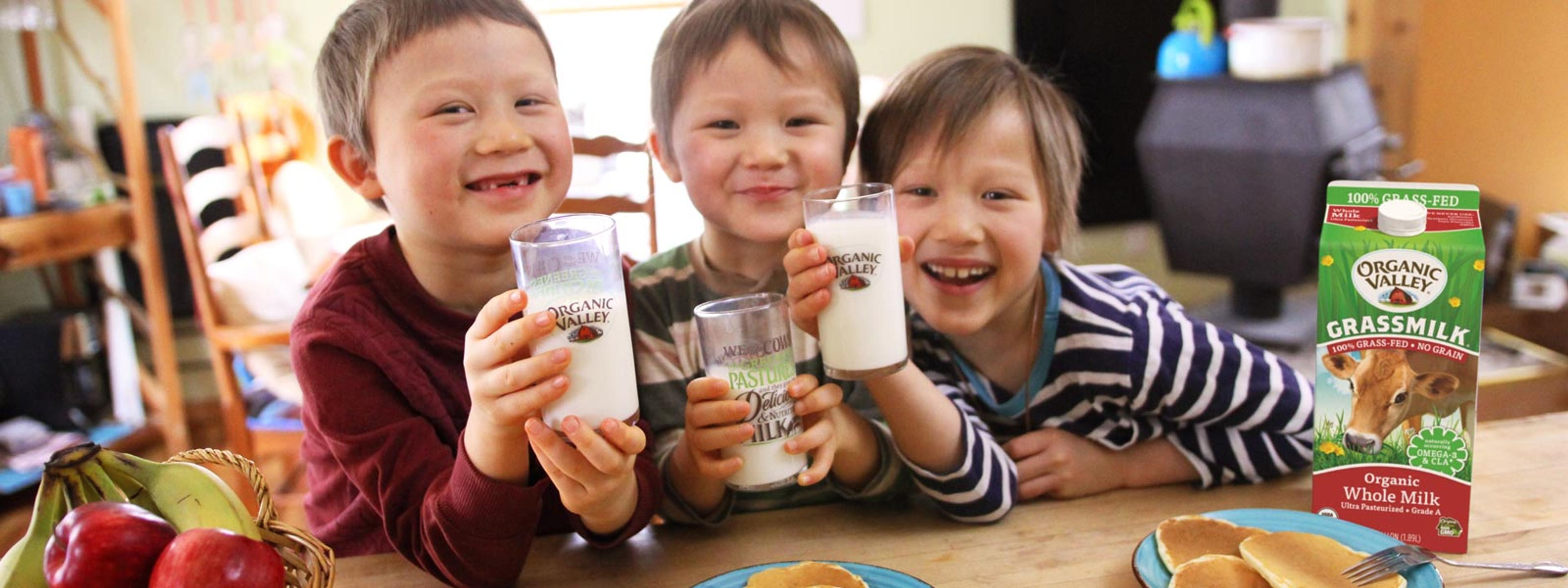 Asian children smile with glass of milk in hand.