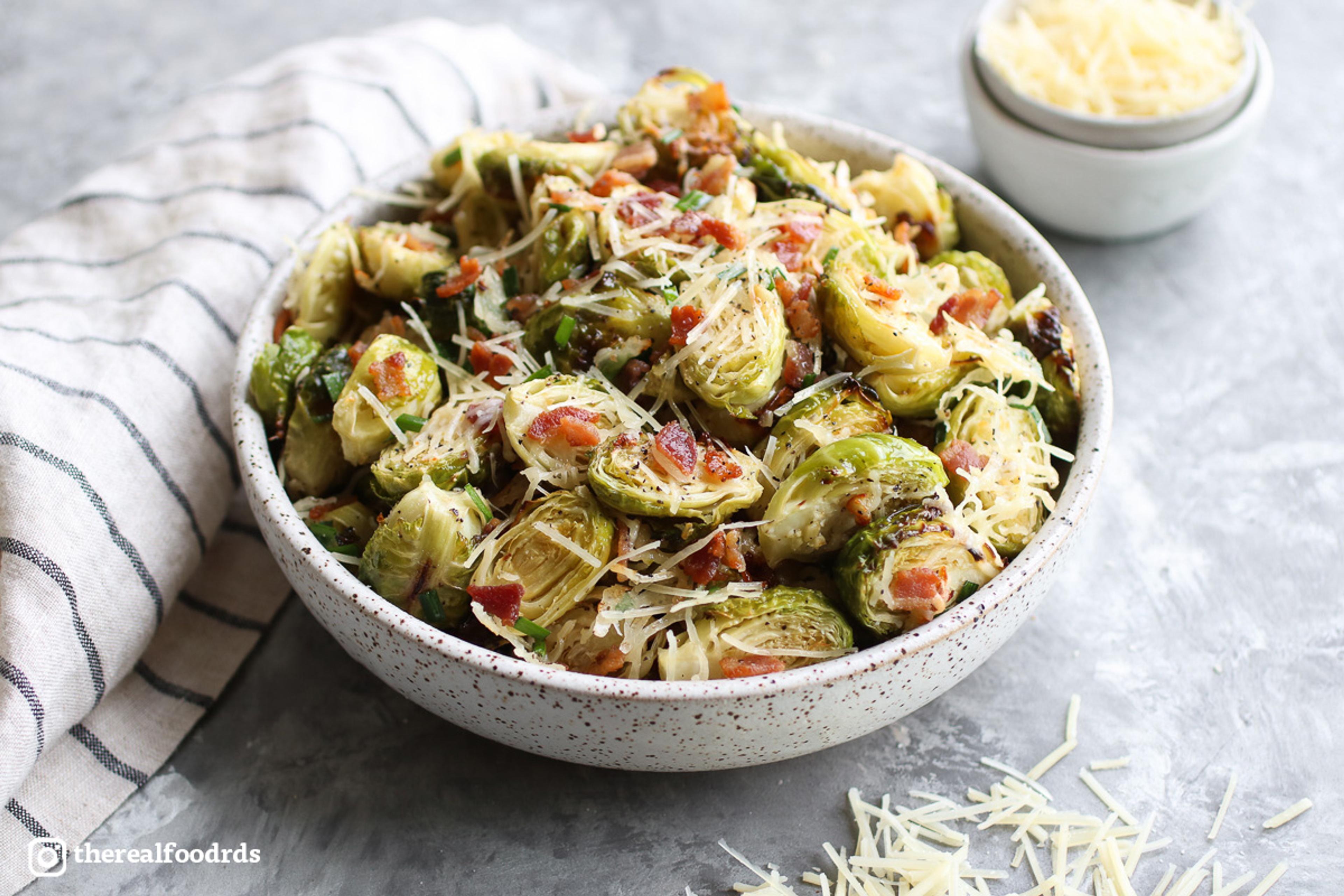 A bowl of roasted Brussels sprouts artfully garnished with shredded cheese and bacon crumbles.