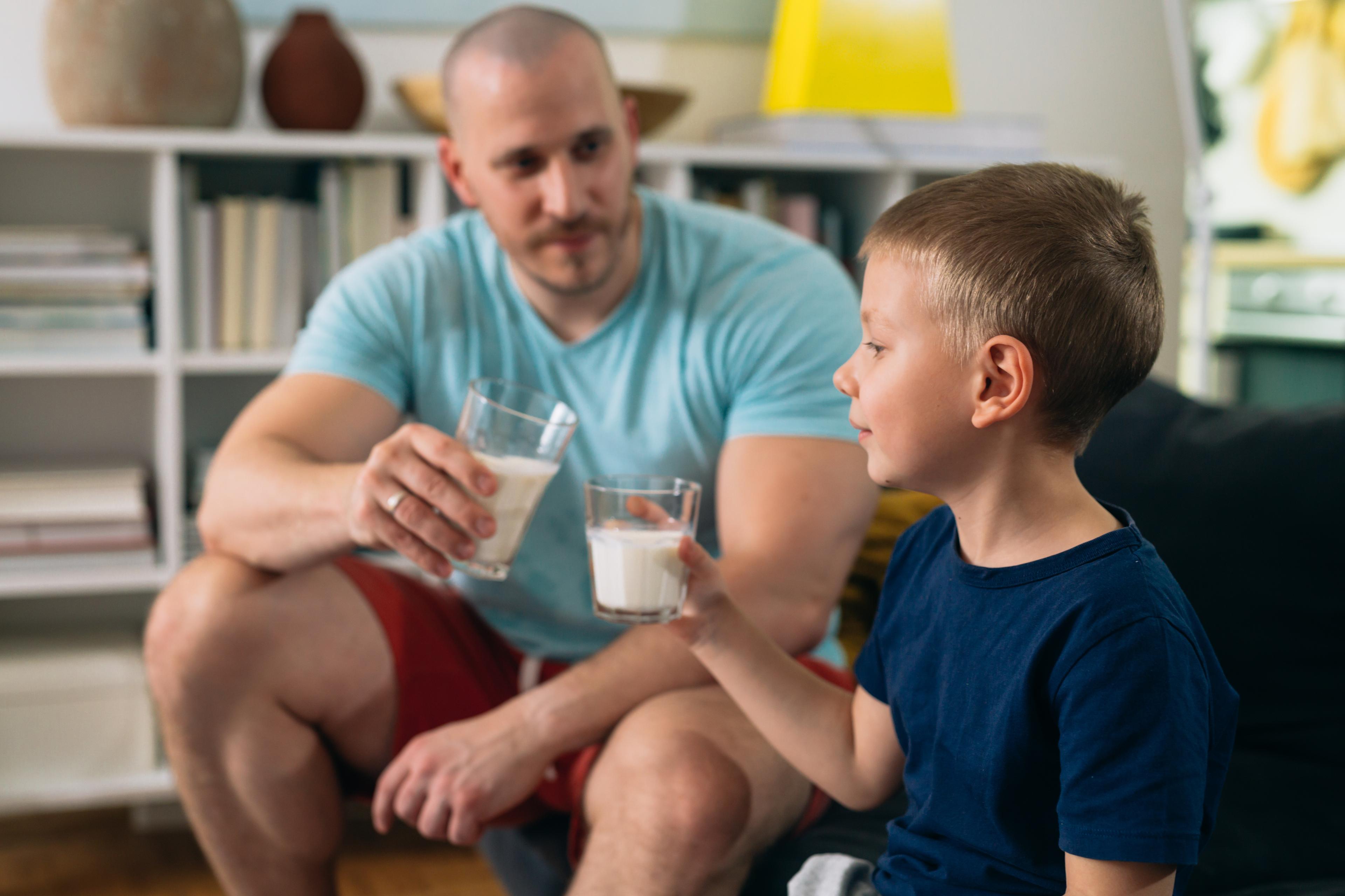 A dad and son drink milk in their living room.