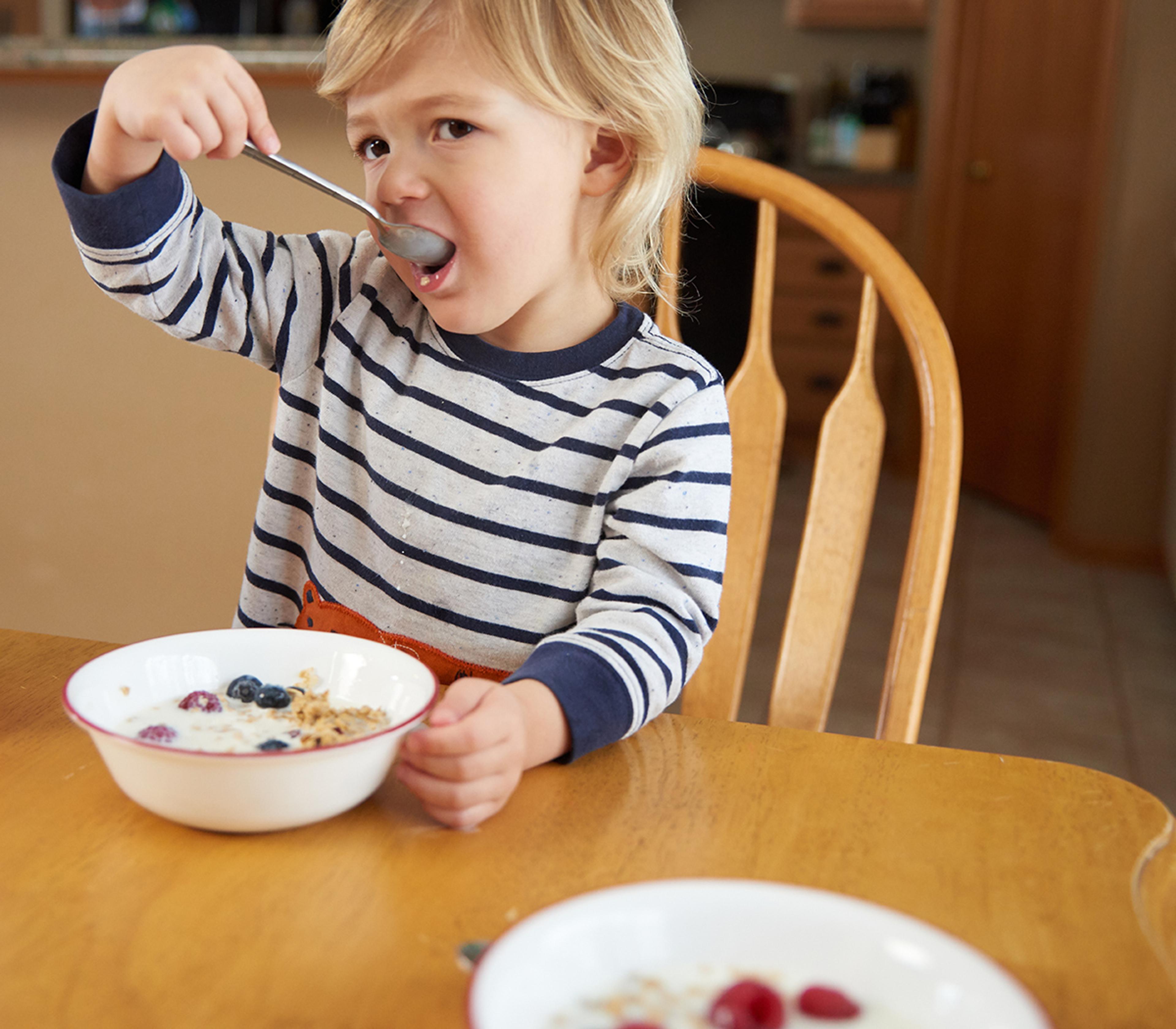 A little boy eats a bowl of cereal topped with fresh berries.