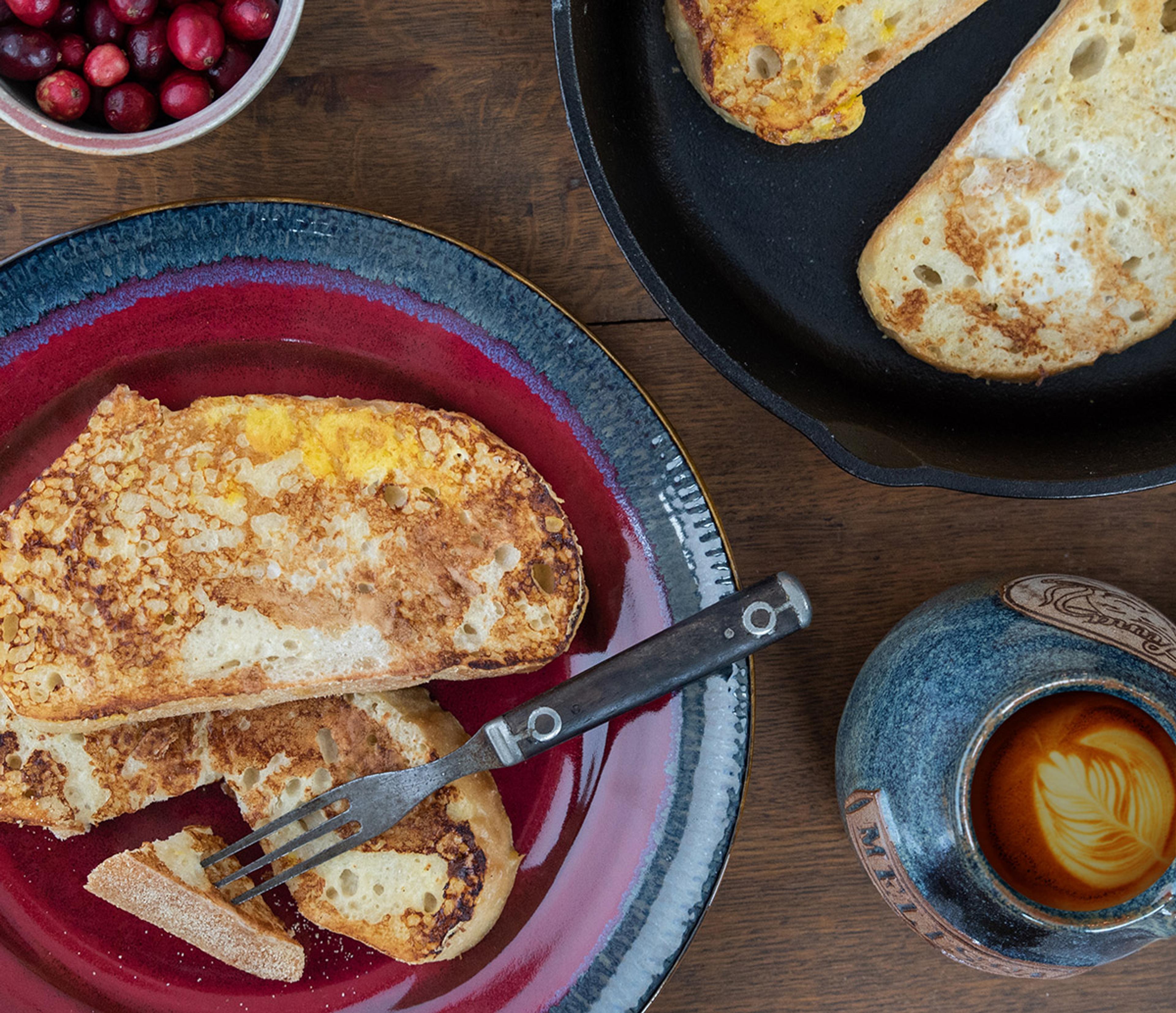 Eggnog french toast on colorful stoneware plates with a cup of coffee nearby.