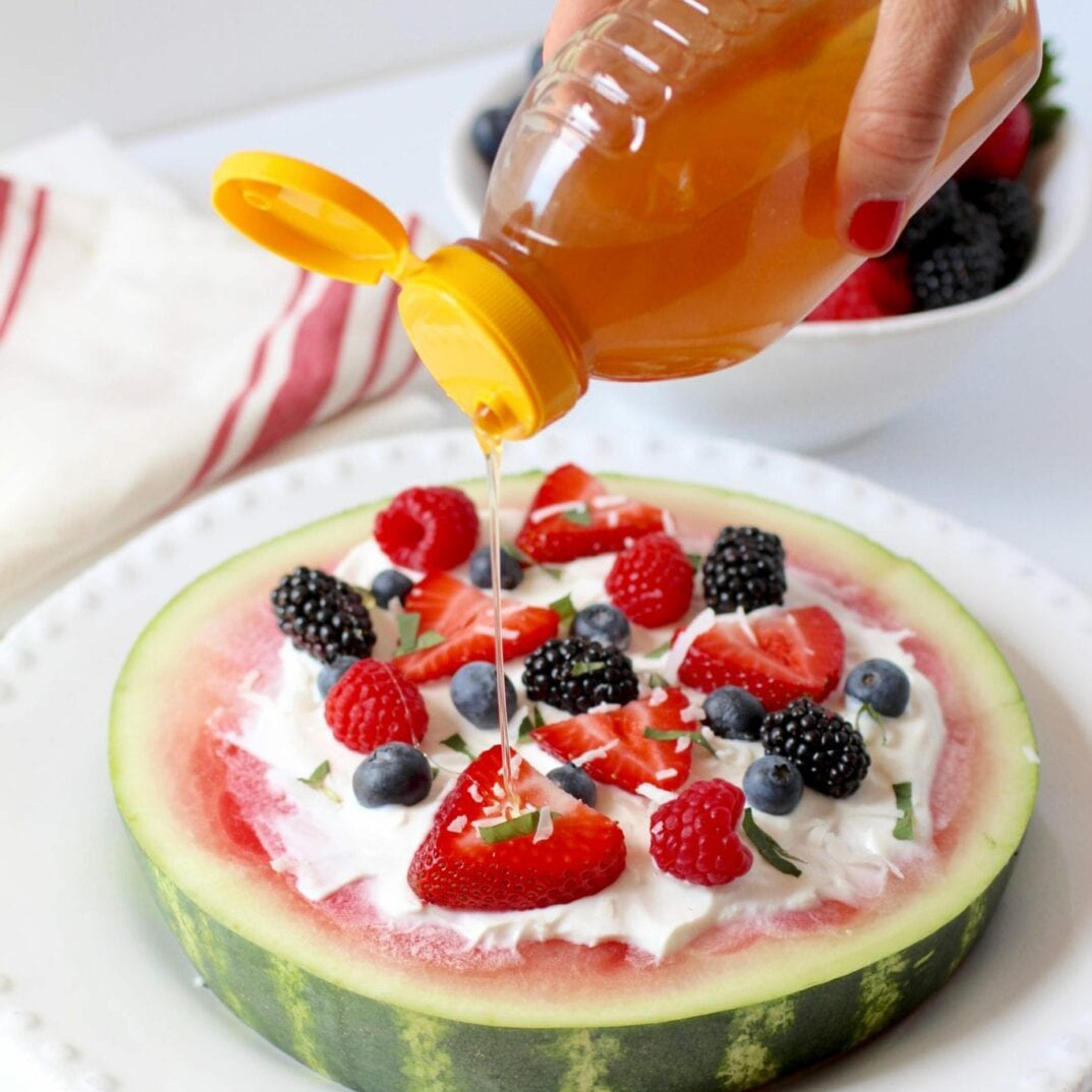 A large slice of watermelon spread with whipped cream, mixed berries, and honey drizzled on top.