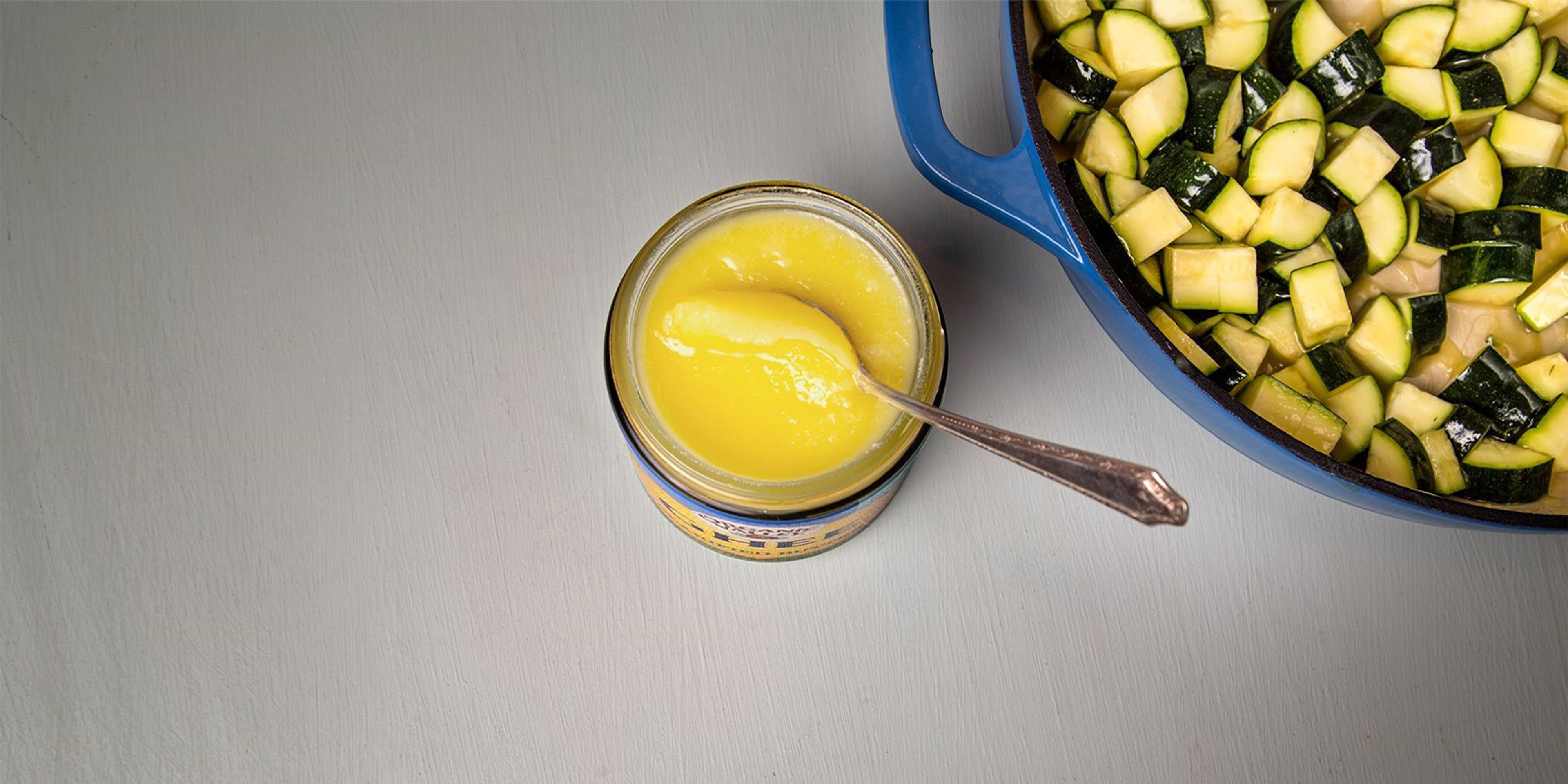 A spoon in a jar of ghee next to a Dutch oven full of veggies.