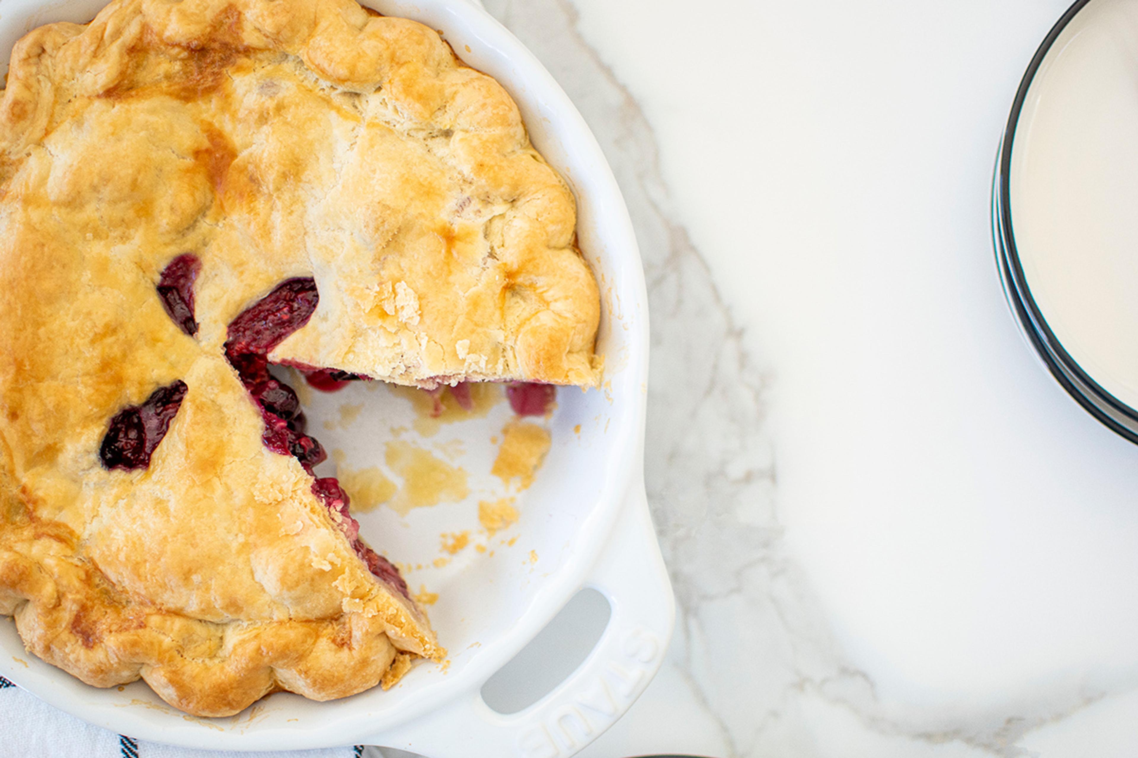Slice of pie cut out of a mouth-watering triple berry pie with a flaky buttery crust.