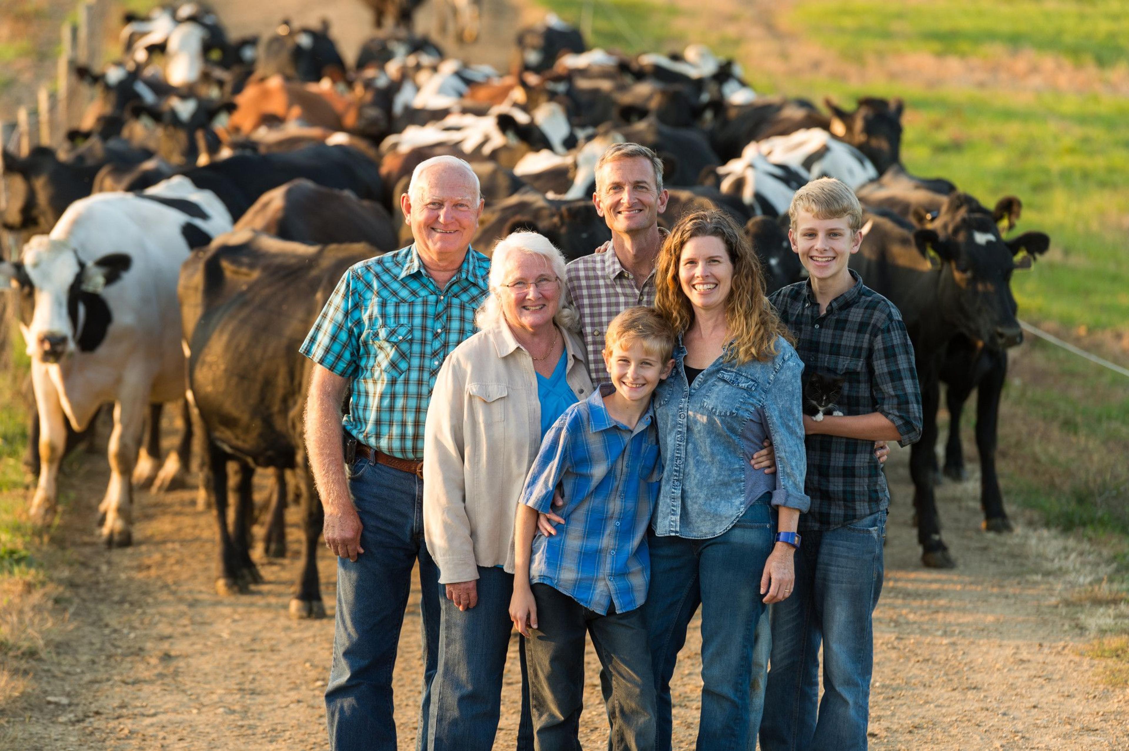 Generations of family farmers stand in front of a herd of cows on their farm in Virginia.