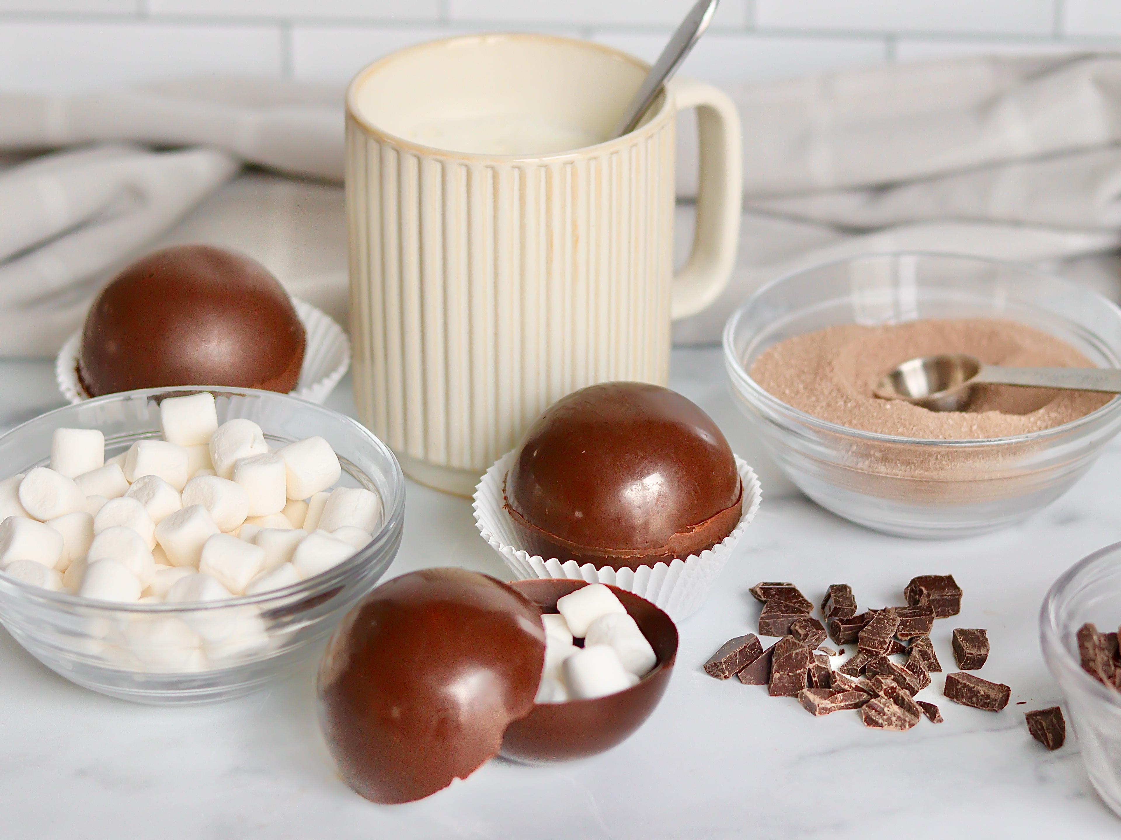 Hot chocolate bombs on a counter with ingredients and marshmallows.